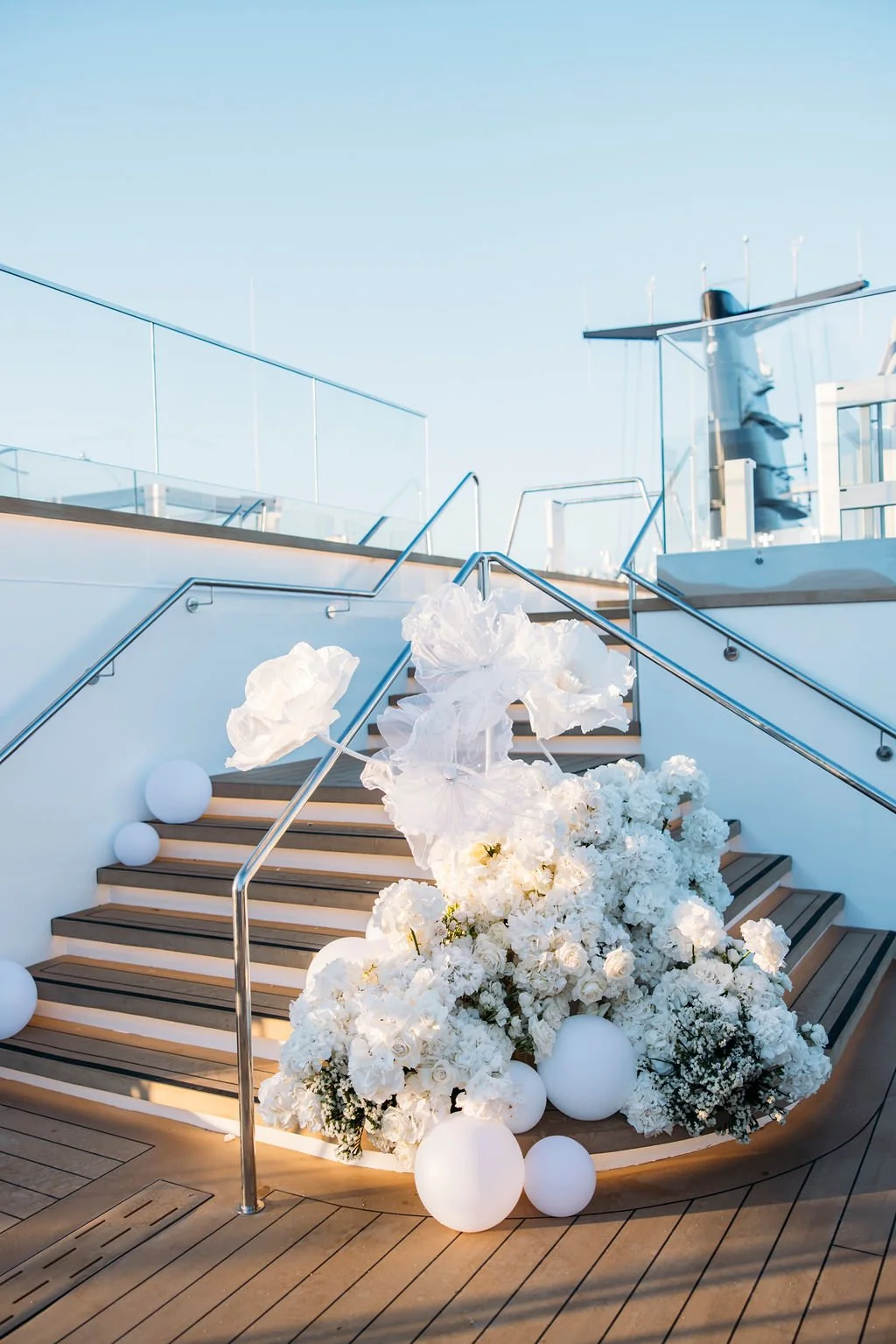 Decorative floral arrangement with white flowers and globes on a staircase, on a yacht deck, during daytime.