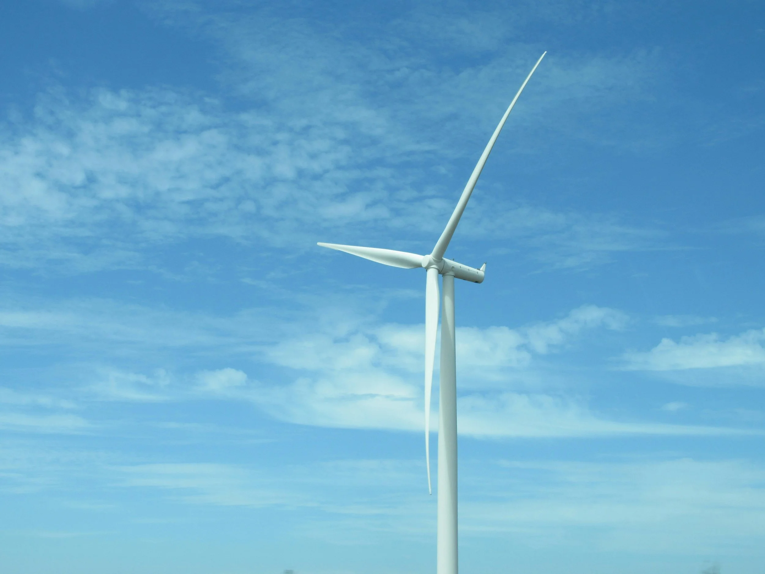 A wind turbine with three blades on a clear blue sky.