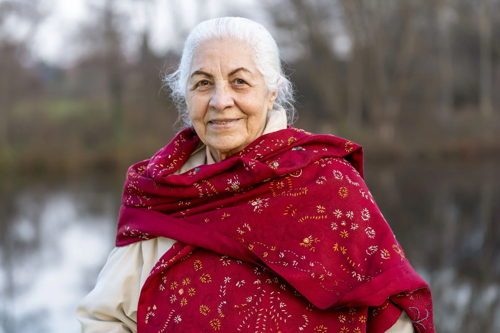 Weißhaarige Frau mit rotem Tuch lächelt in die Kamera