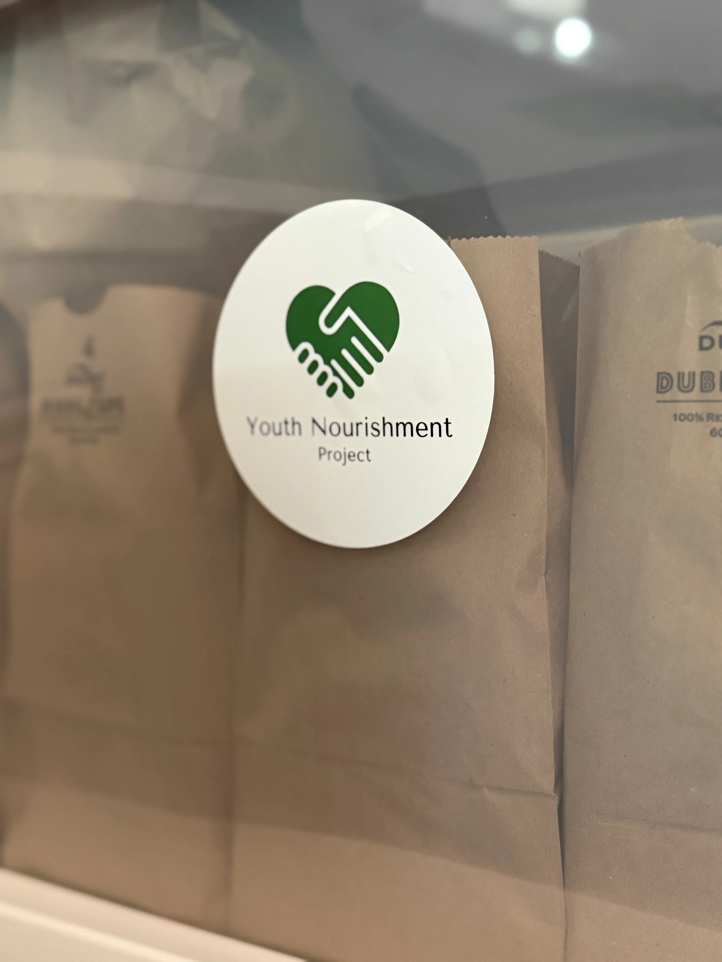 Youth Nourishment Project sticker on the outside of a donation bin, filled with teen snack bags