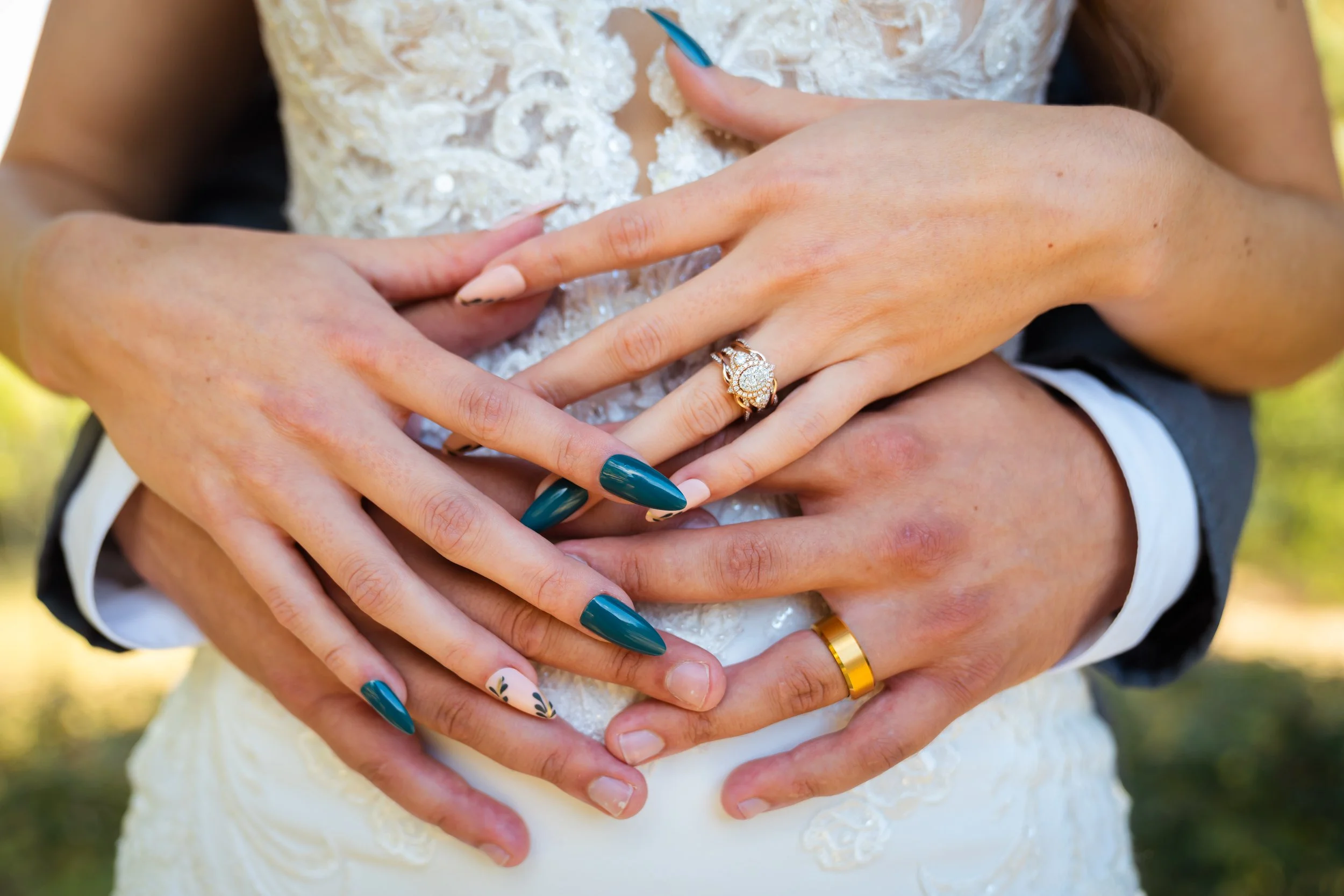 Close-up of hands, decorated with rings, forming a heart shape over the wedding dress.