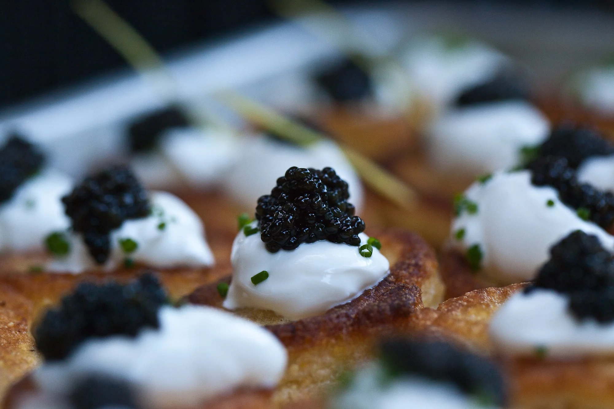 Close-up of canapés topped with dollops of cream and black caviar, garnished with chopped chives, arranged on a serving tray.