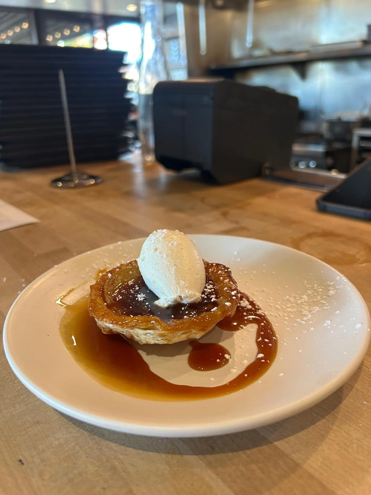 Dessert with caramel sauce, vanilla ice cream, powdered sugar, on a white plate on a wooden table in a restaurant.