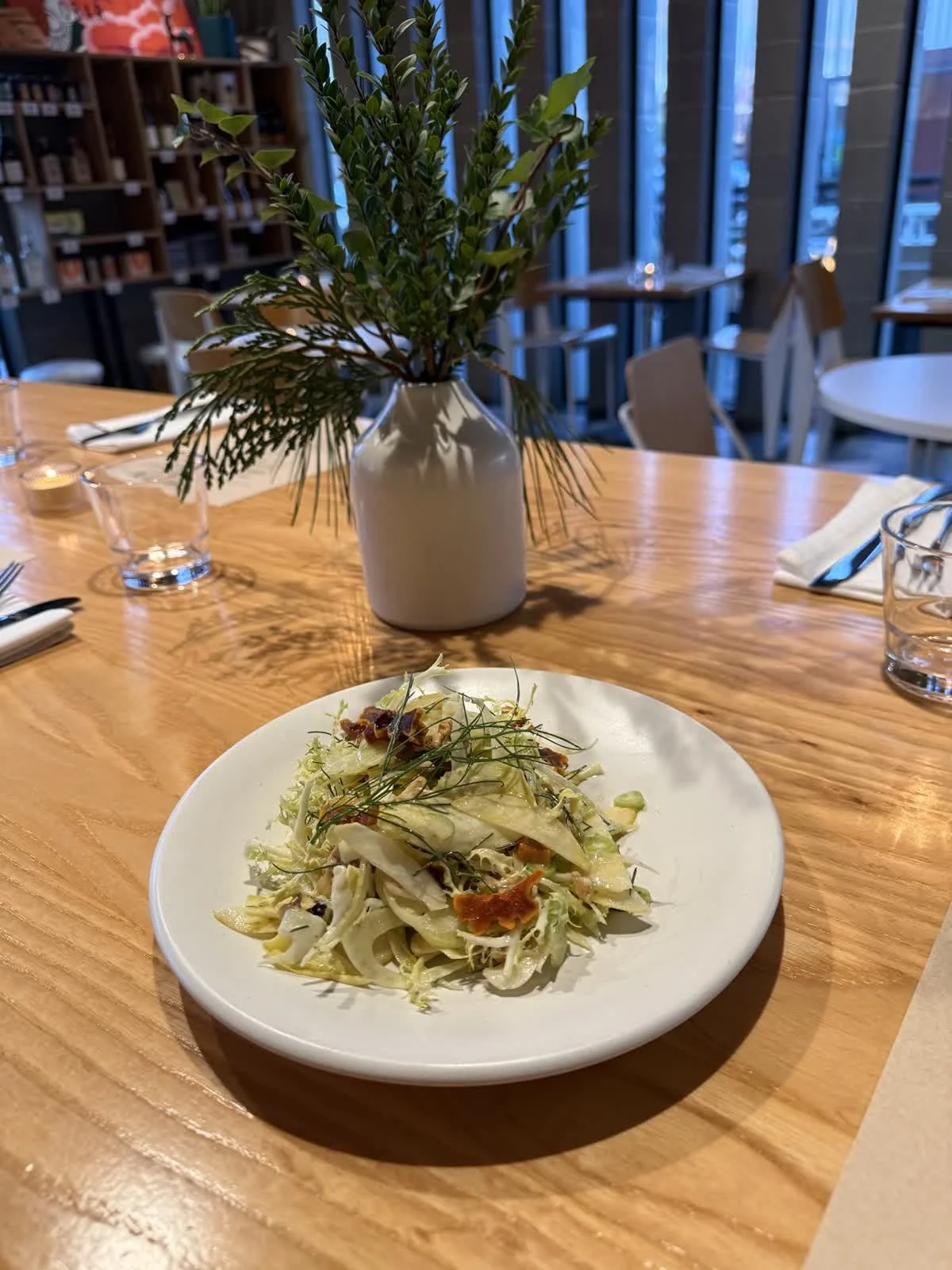A plate of salad with lettuce, herbs, and bacon bits on a wooden table.