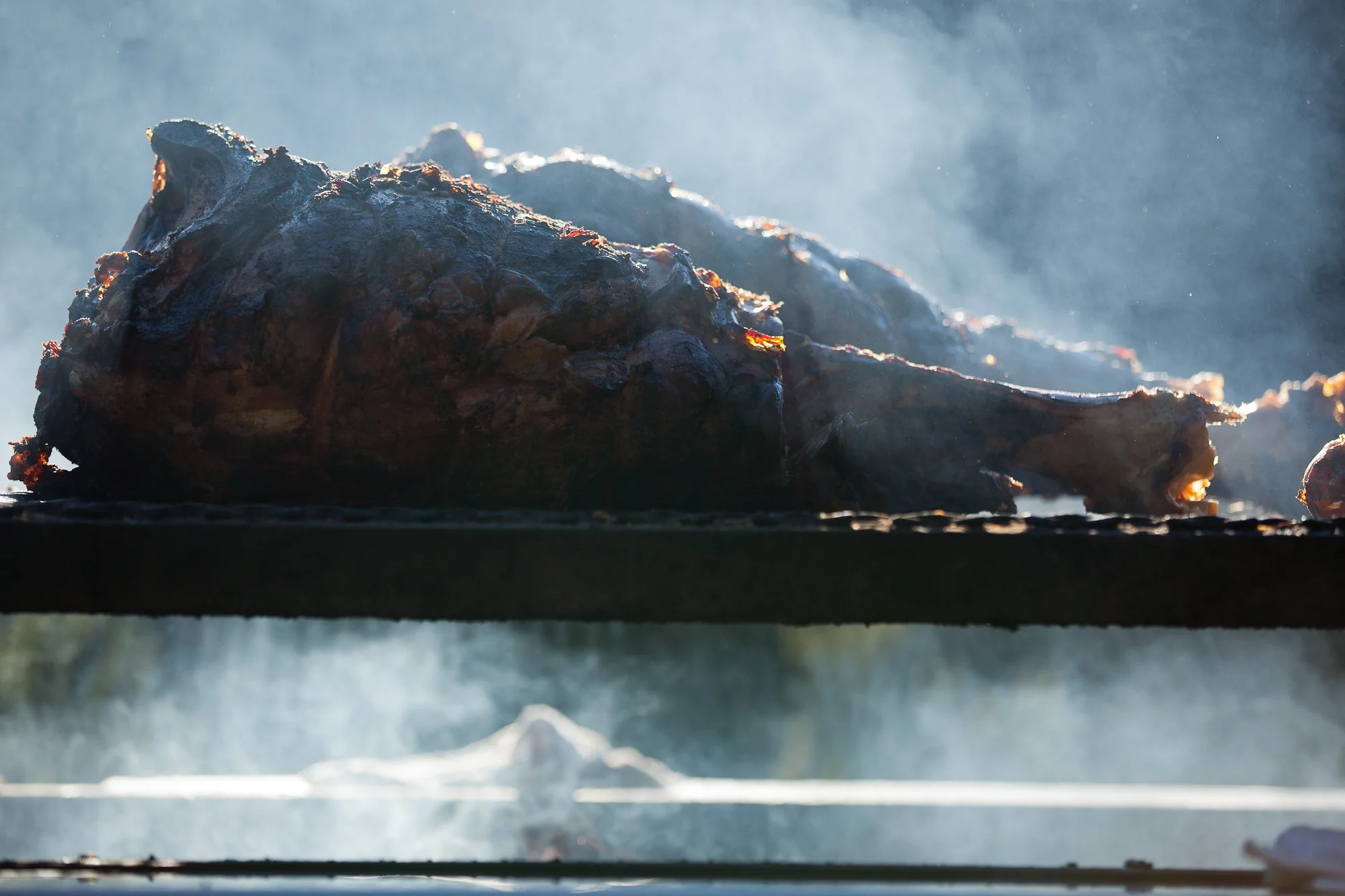 A close-up of a large piece of meat being cooked on a grill, with smoke rising around it.