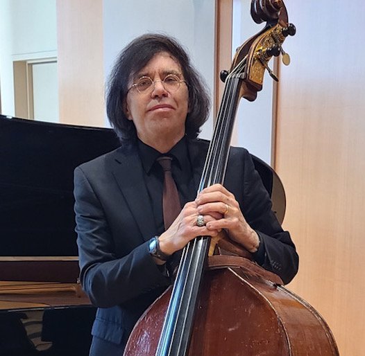Man in a suit holding a double bass in a music room.