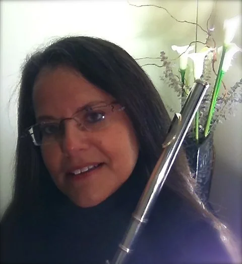Woman with dark hair and glasses smiling in front of a floral arrangement in a vase.