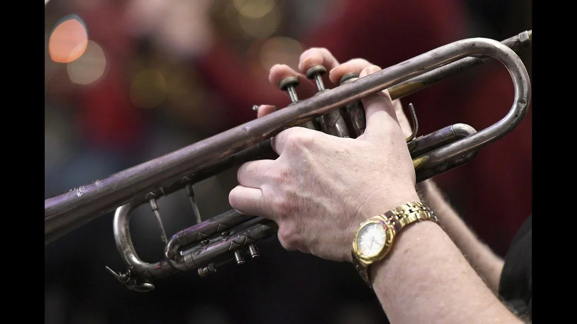 A person's hand holding a silver trumpet, wearing a gold wristwatch.