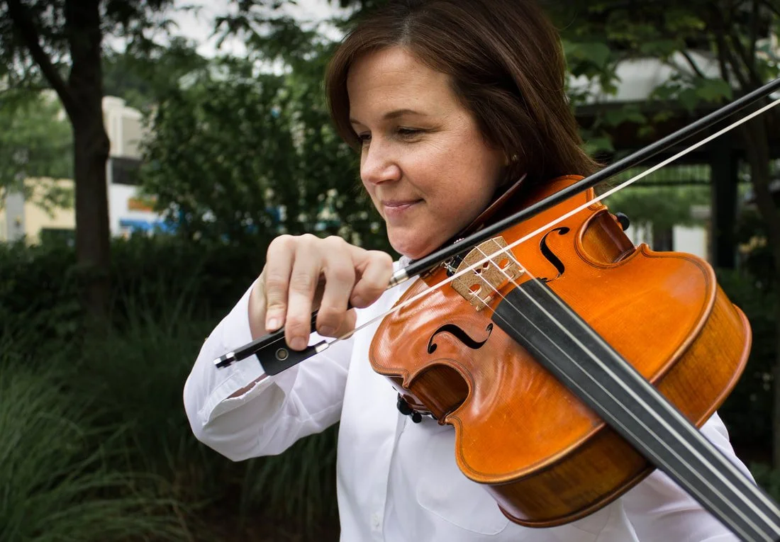 A woman playing a violin outdoors.