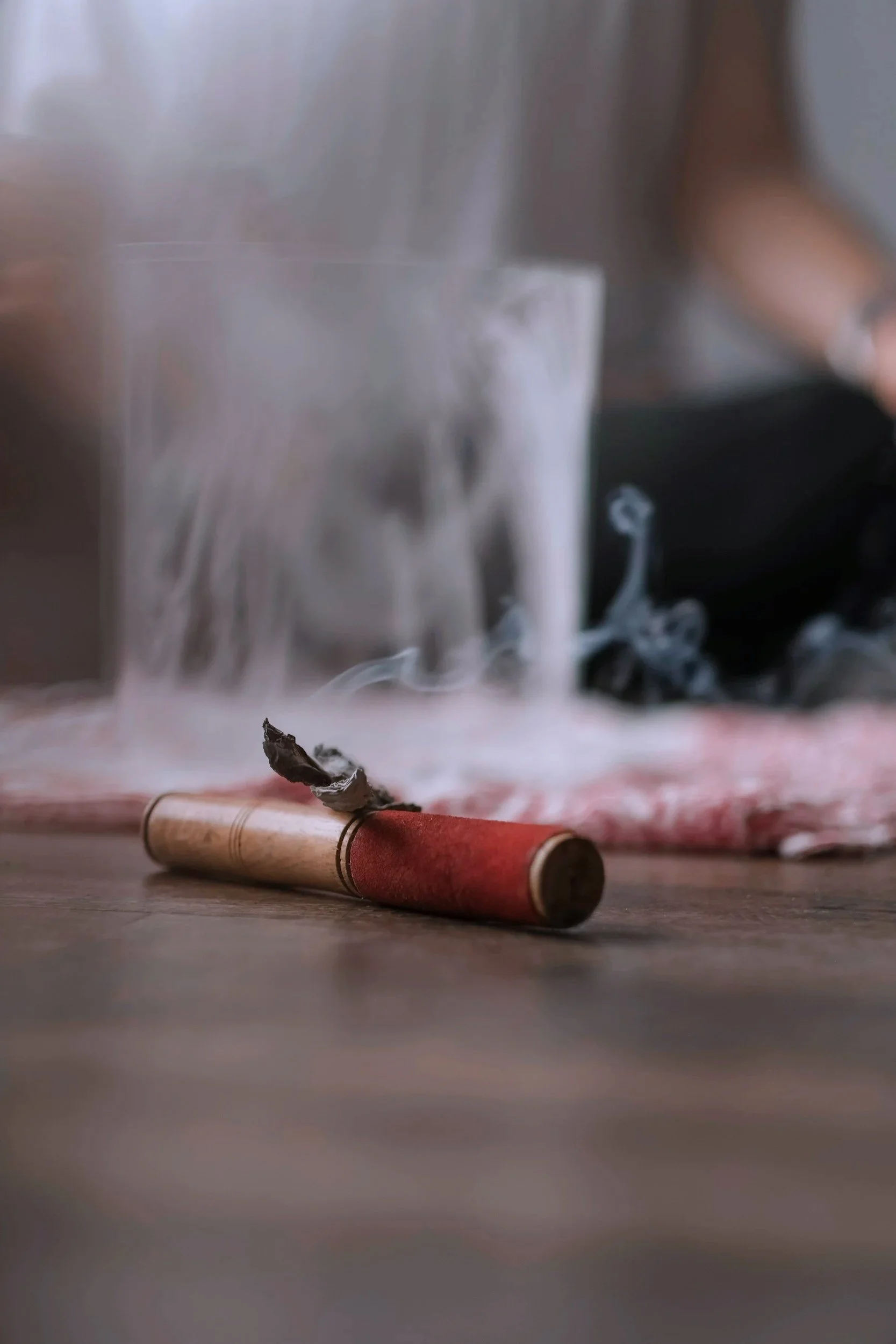 A partially burned red firework lying on a wooden surface with smoke rising from the charred remains.