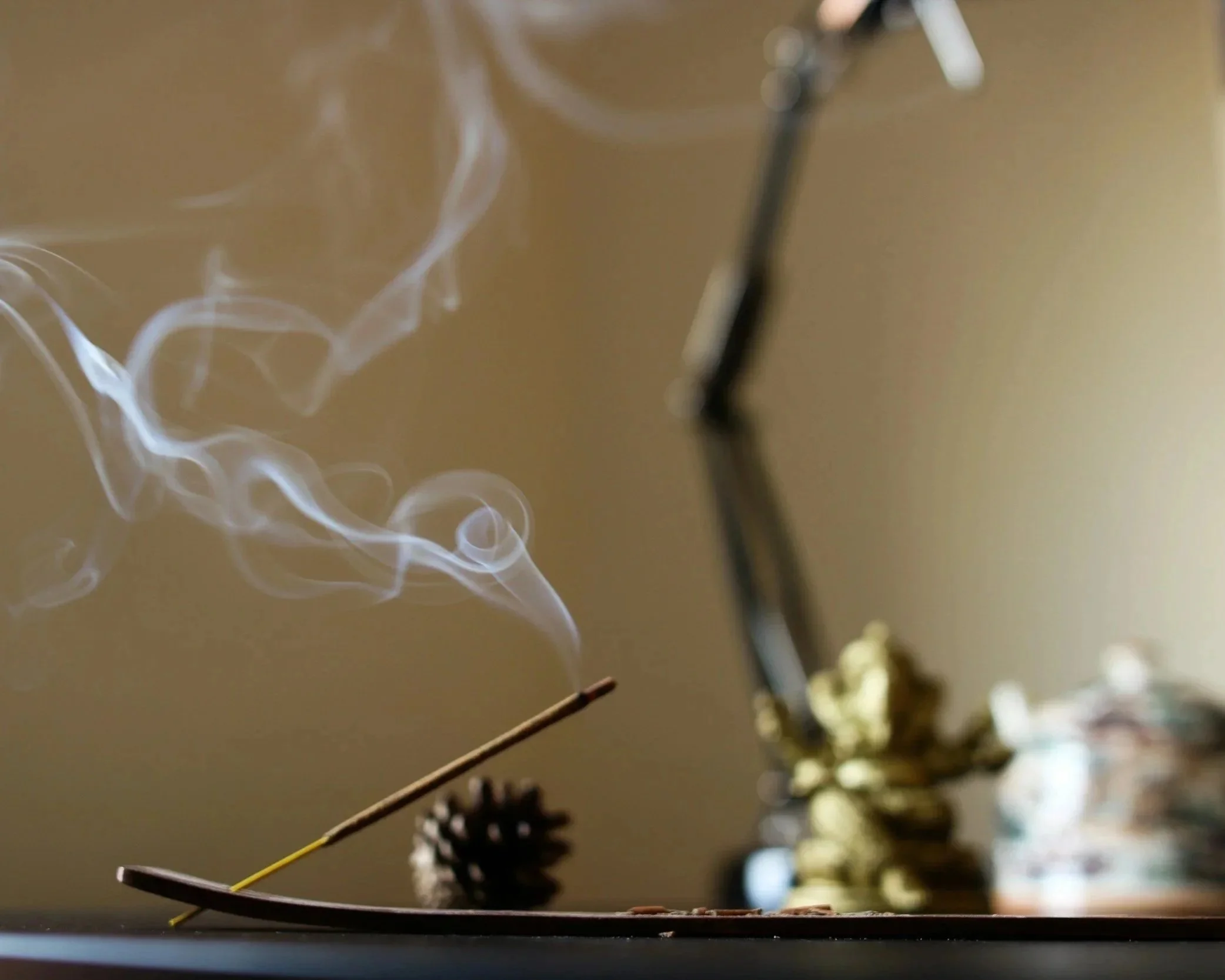 Close-up of incense sticks burning, with smoke rising in a smoke ring against a beige background.
