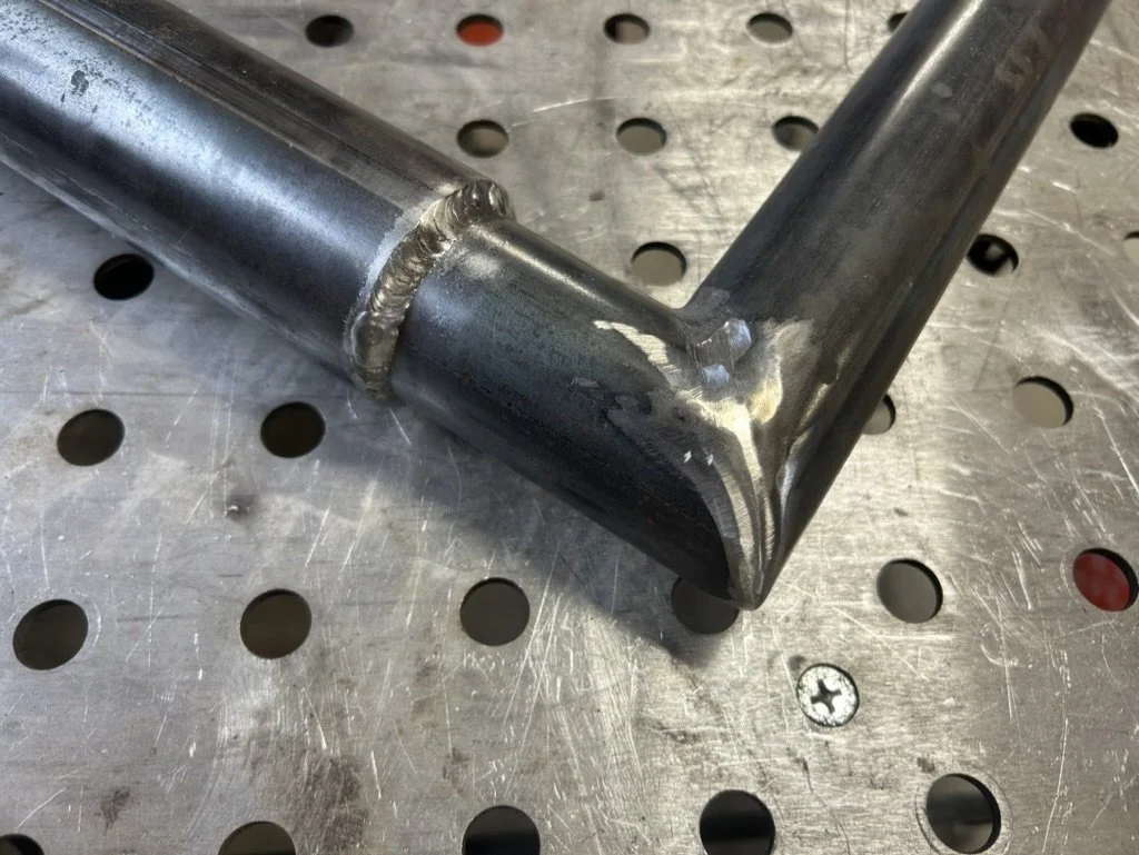 Close-up of a welded metal frame on a perforated metal work surface.