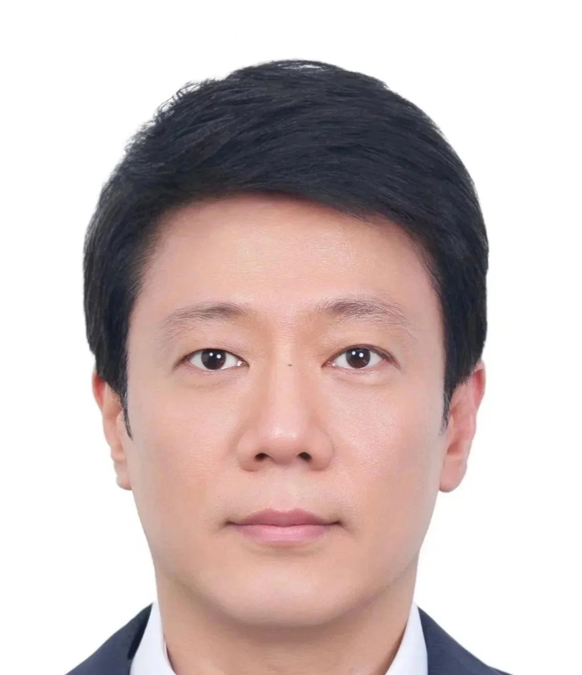 A man with short black hair wearing a gray blazer and patterned shirt, standing against a two-tone blue and yellow background.