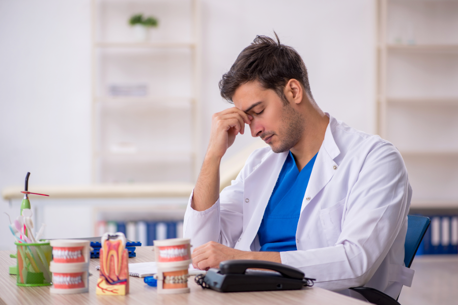 photograph of a male dental professional sitting at his office desk holding the bridge of his nose