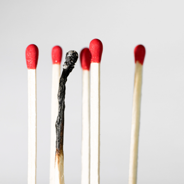 Several matchsticks with red heads, one burnt out and blackened, on a plain background.