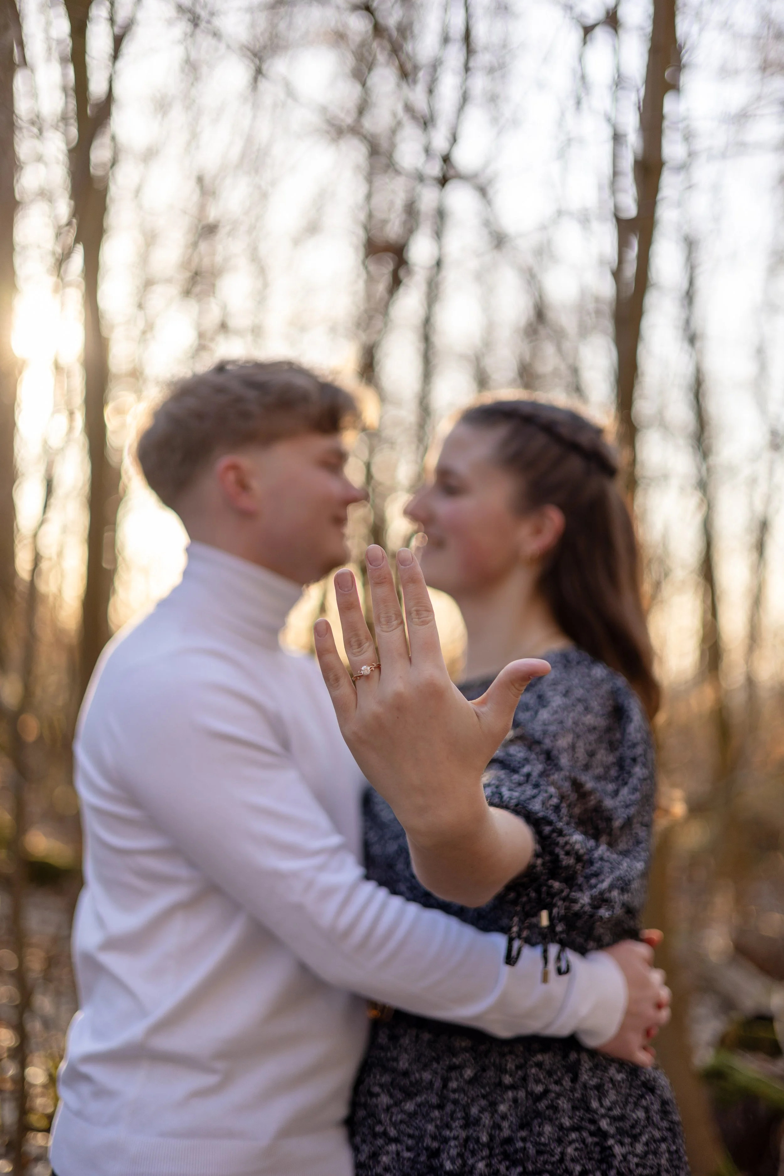 Ein Mann und eine Frau stehen sich gegenüber in einem Wald, sie halten die Hände in die Luft und zeigen auf ihre Hände, im Hintergrund sind Bäume und Sonnenlicht.