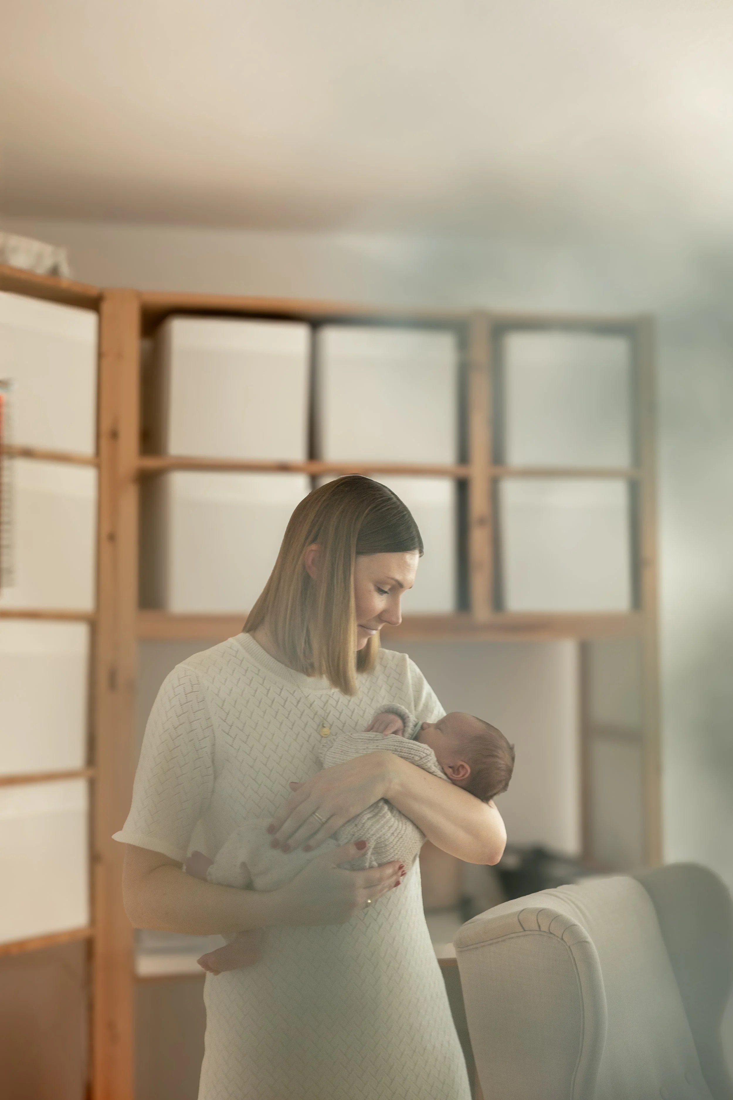Frau hält ein neugeborenes Baby in den Armen im Wohnzimmer.
