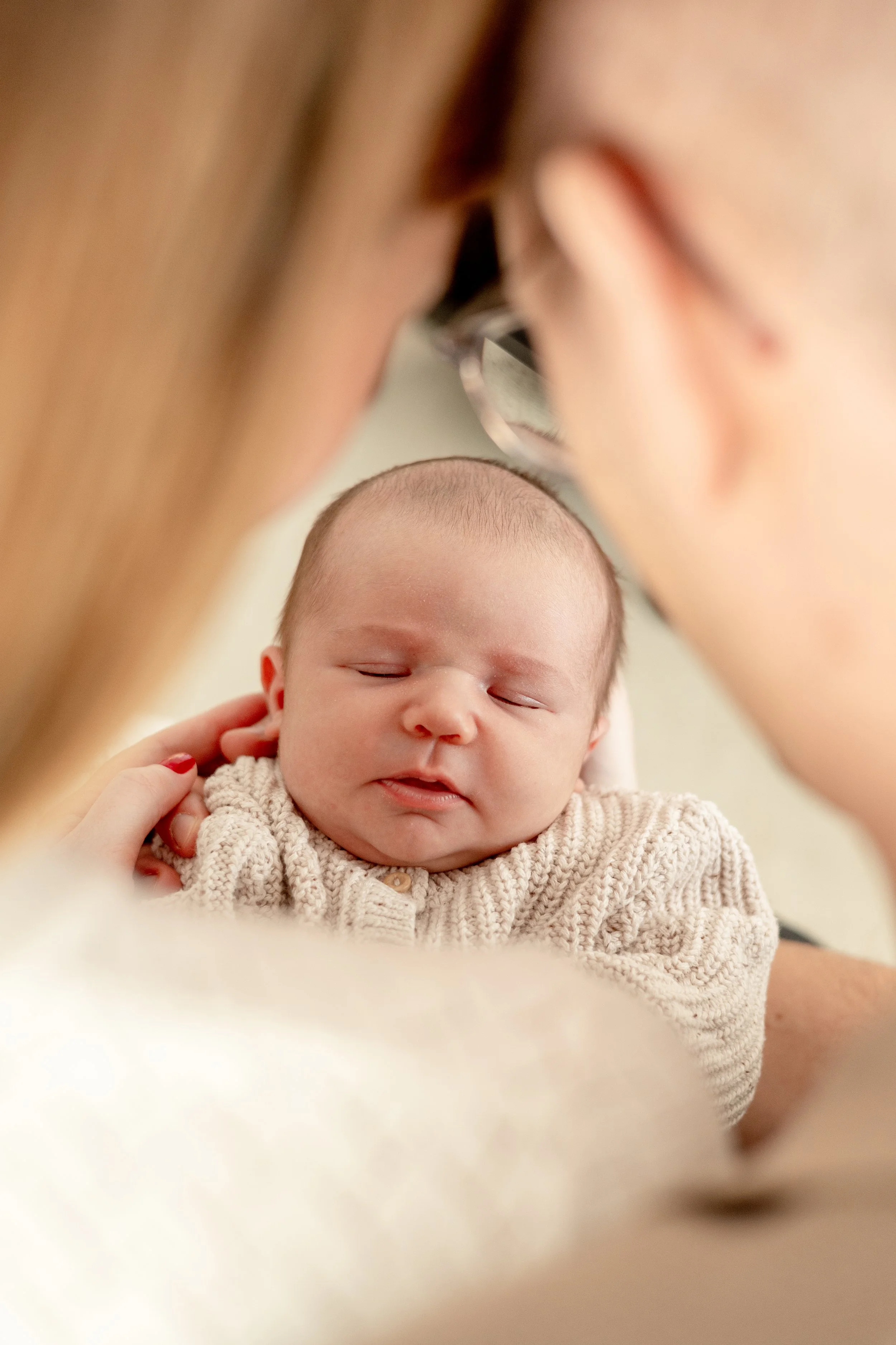 Ein Baby mit geschlossenen Augen, das auf einem weichen, hellen Stoff liegt, während ihm jemand sanft an den Haaren streichelt. Die Person trägt rotem Nagellack.