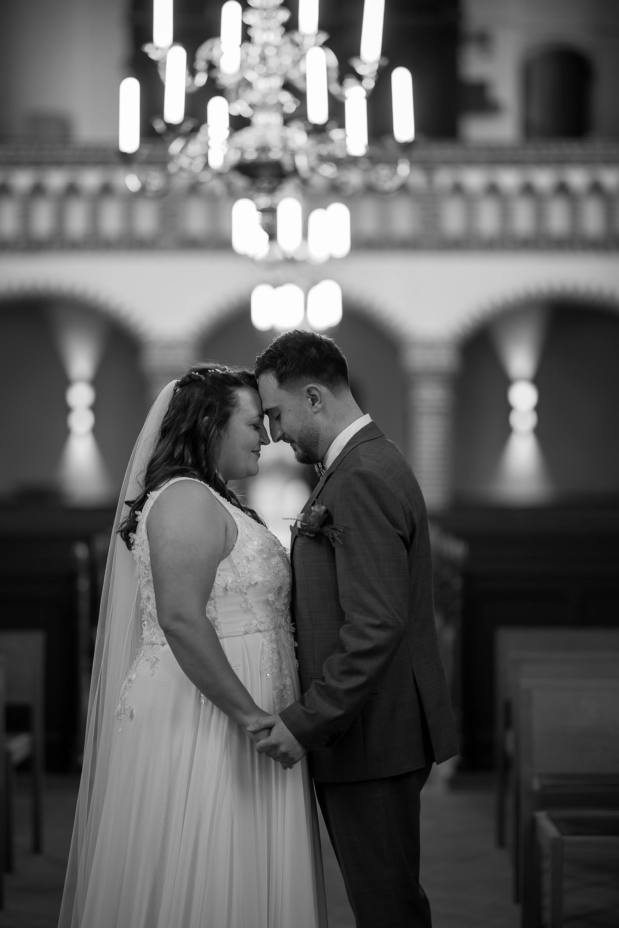 Ein Brautpaar in einem Trauzimmer, das sich an den Händen hält und sich berührt, in einer emotionalen Geste während ihrer Hochzeit.