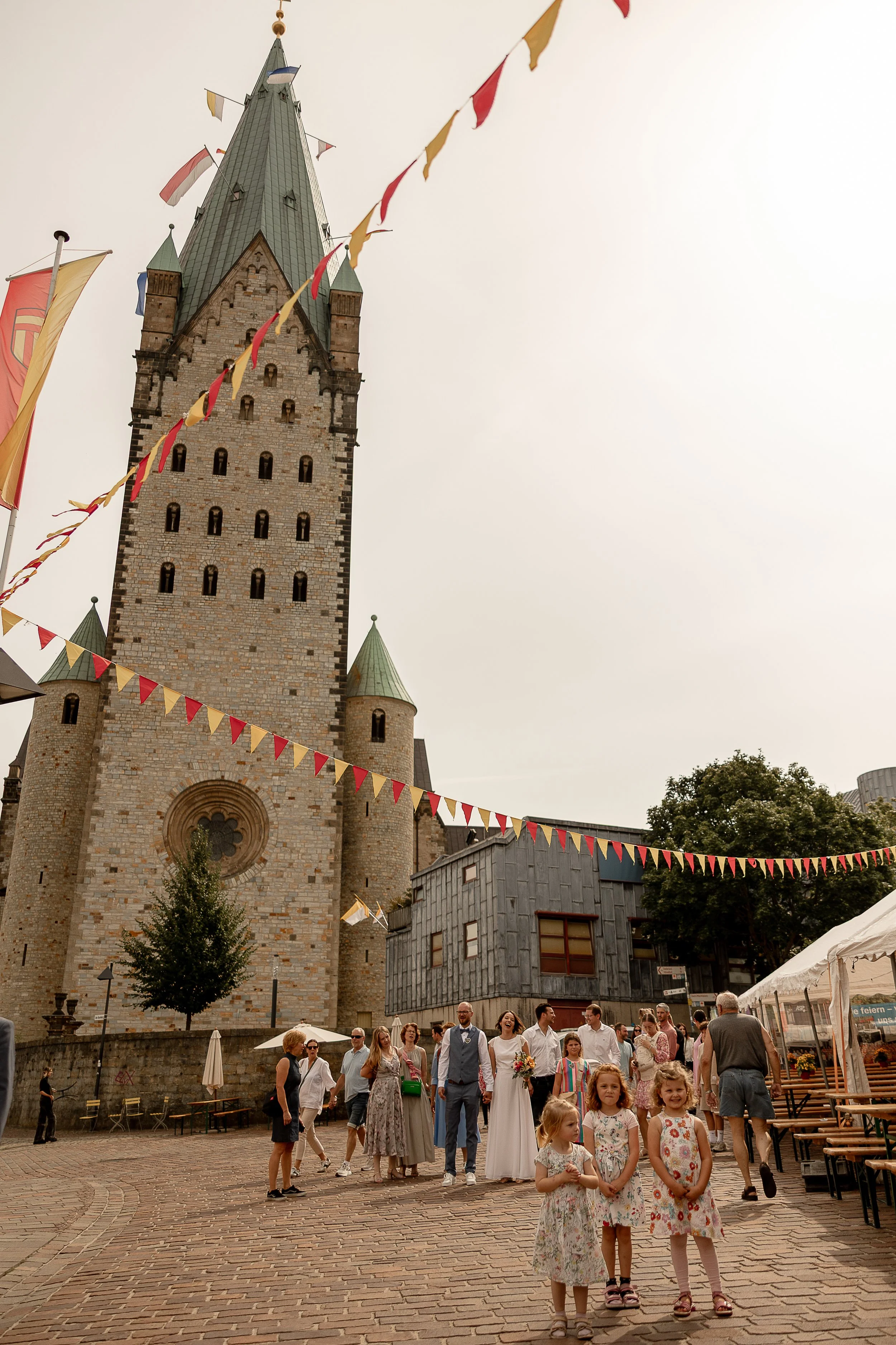Eine Gruppe von Menschen, darunter Kinder und Erwachsene, versammelt sich vor einer mittelalterlichen Burg mit einem hohen Turm und bunten Dekorationen, wahrscheinlich bei einer Veranstaltung oder Feier im Freien.