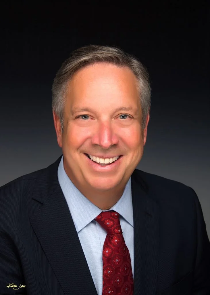 Smiling man in suit with red tie against dark background