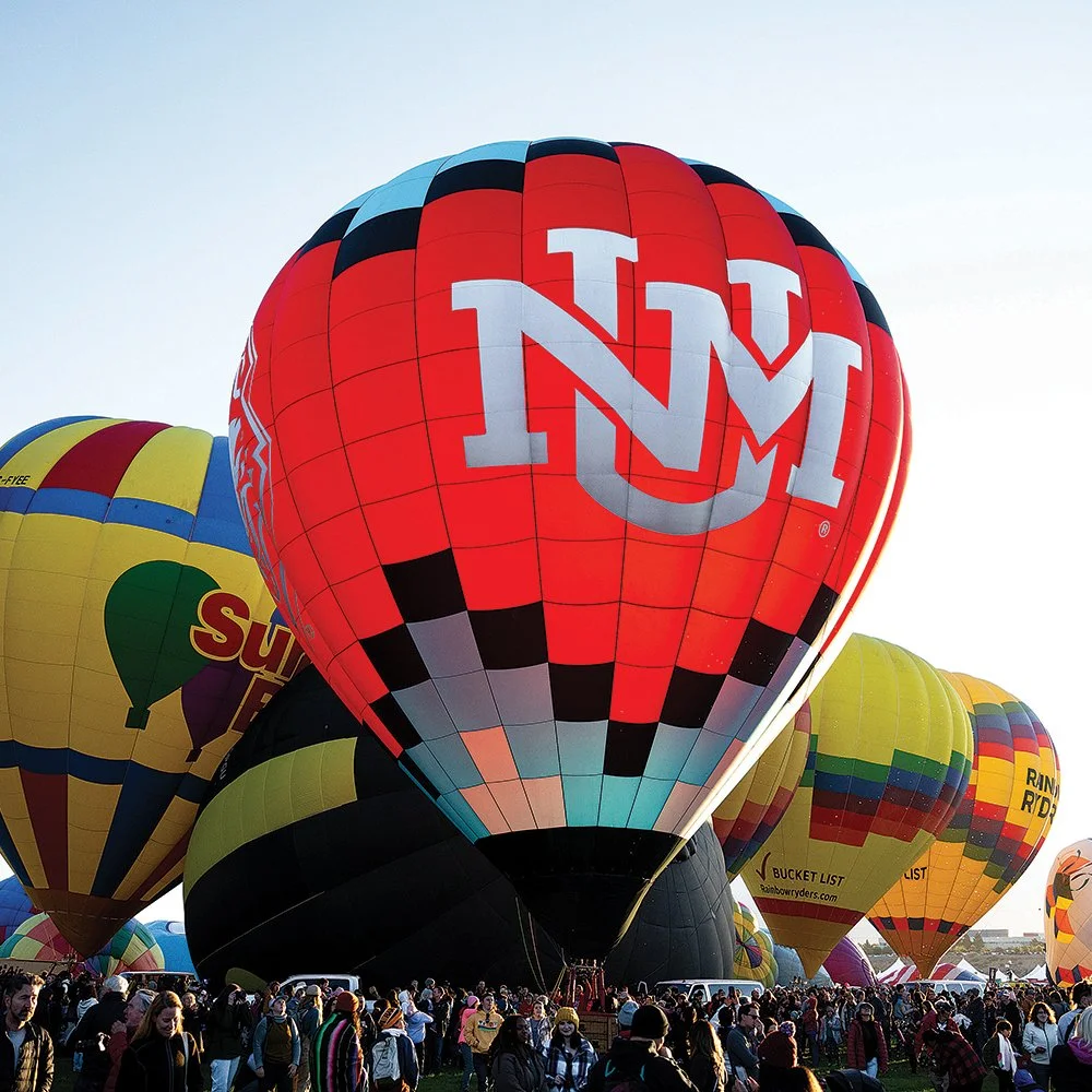 Multiple colorful hot air balloons with a crowd of people at a hot air balloon festival.