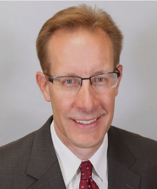 Professional headshot of a middle-aged man with glasses, light brown hair, wearing a dark suit, white shirt, and red tie, smiling.