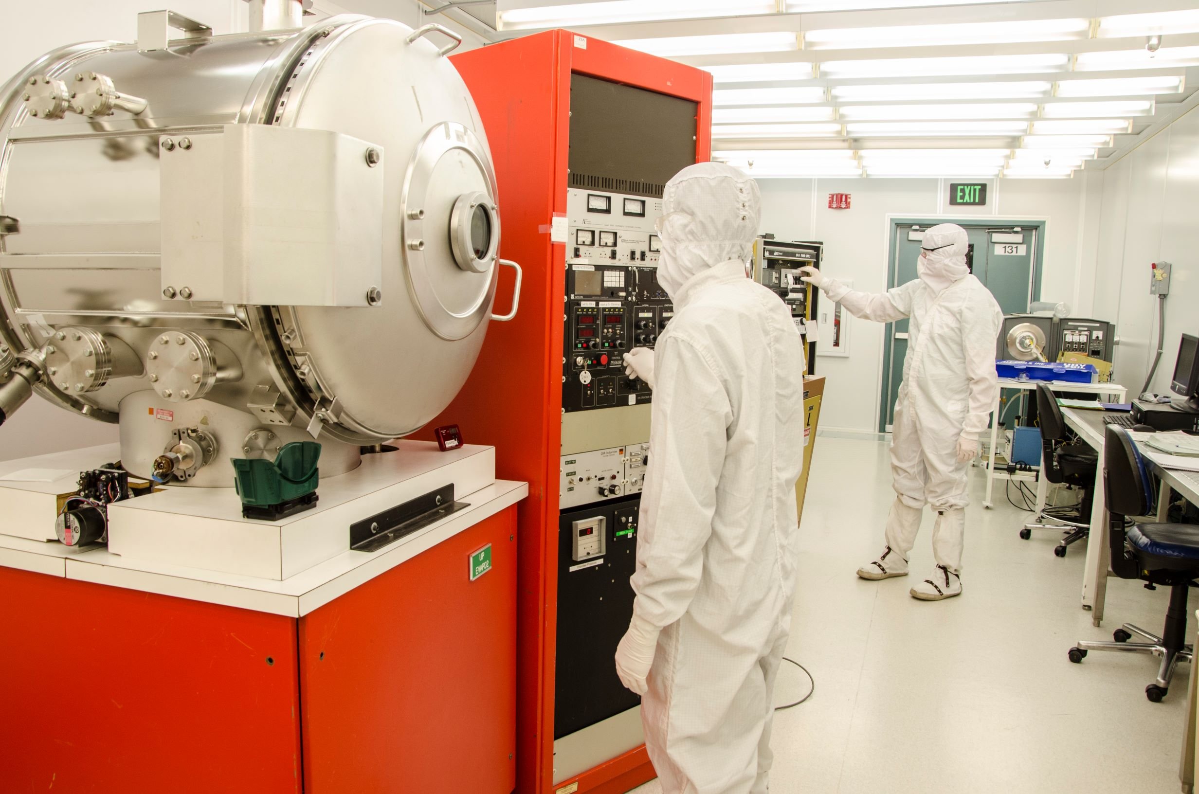 Scientists in cleanroom suits working with a large scientific instrument in a laboratory.