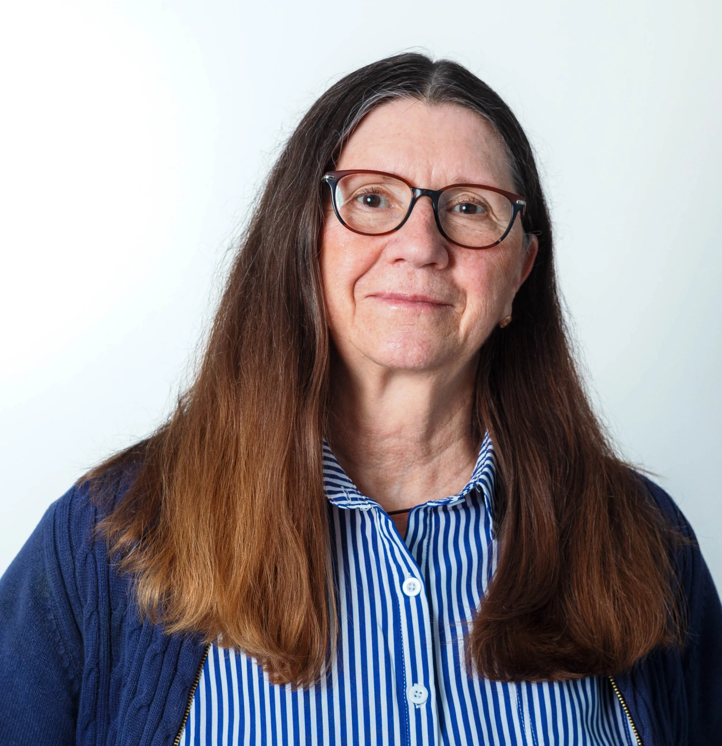A young woman smiling outdoors, surrounded by green foliage.