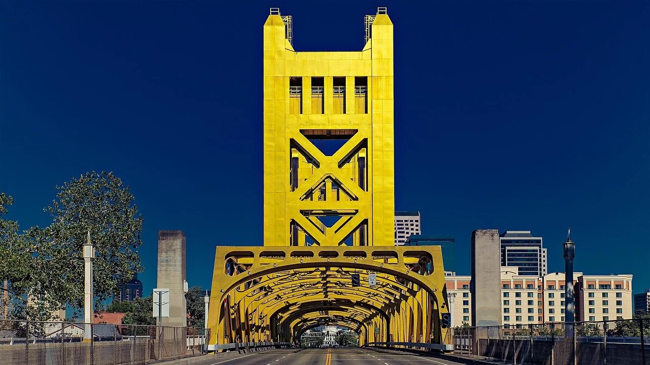 The Tower Bridge in Sacramento, California, painted yellow, with a modern cityscape in the background.