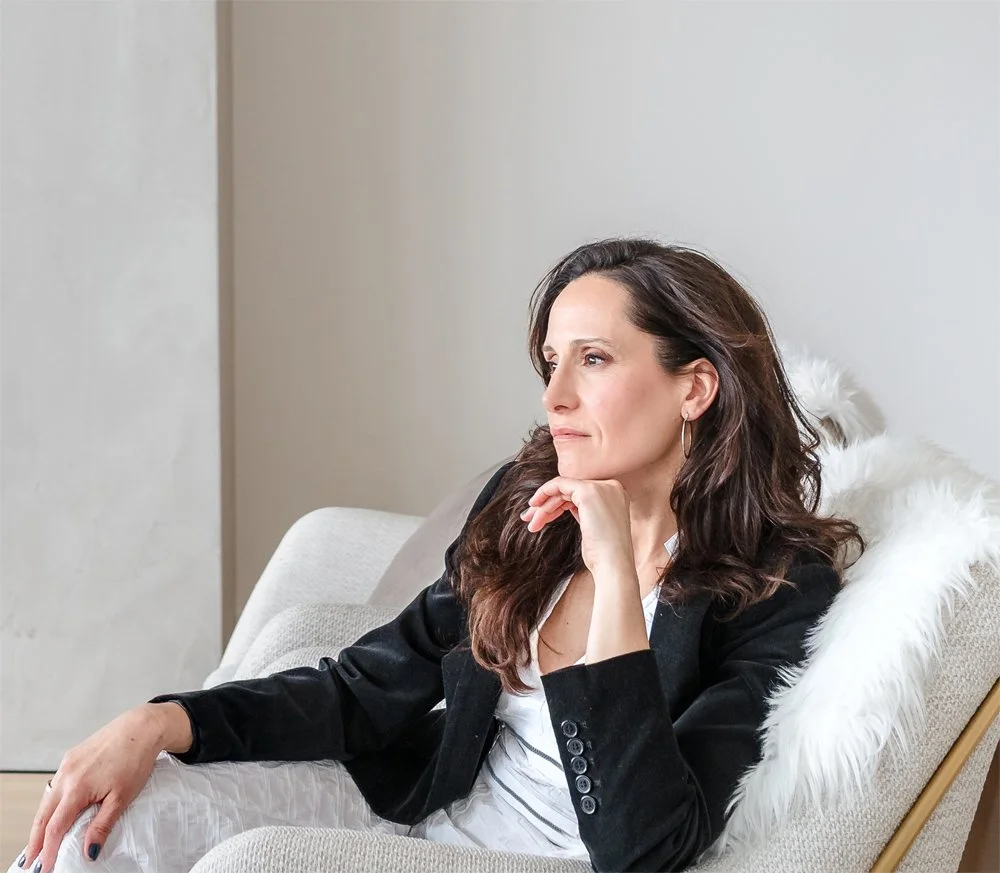 Elena sitting on a beige golden couch in an elegant and minimalist interior setup