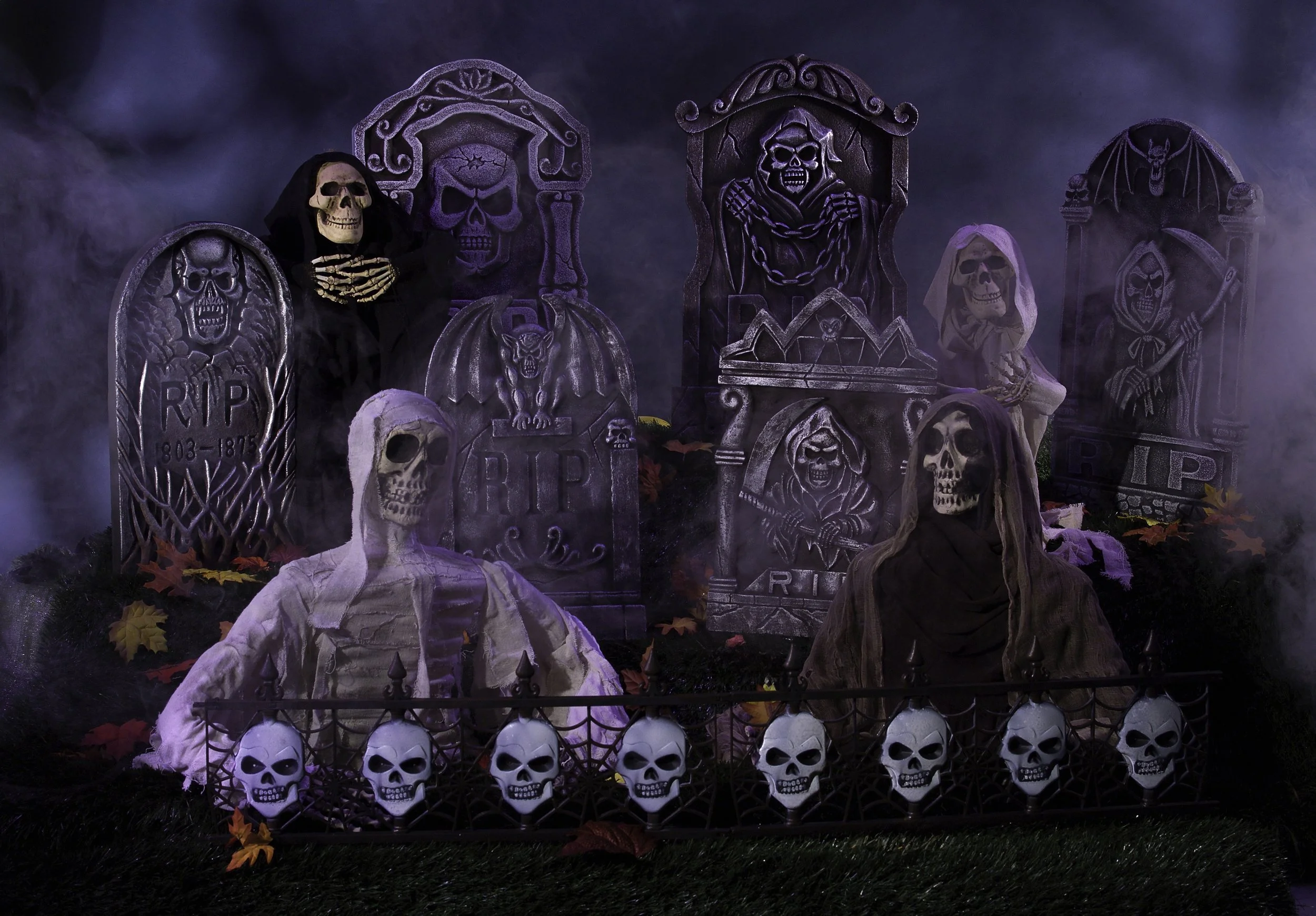 A Halloween display with skeletons and tombstones, including fog, faux autumn leaves, and skull decorations.