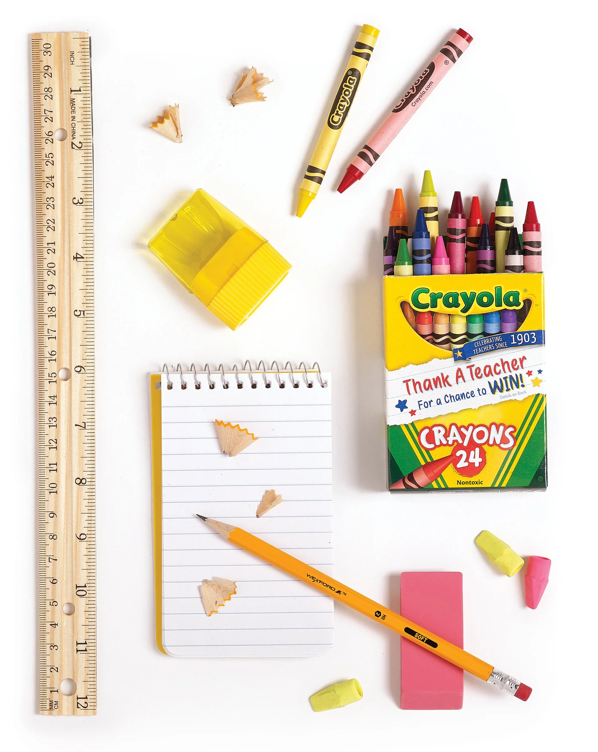 School supplies including a ruler, sharpened pencils, a yellow highlighter, a notebook with pencil shavings, a box of Crayola crayons, and colored chalk on a white background.