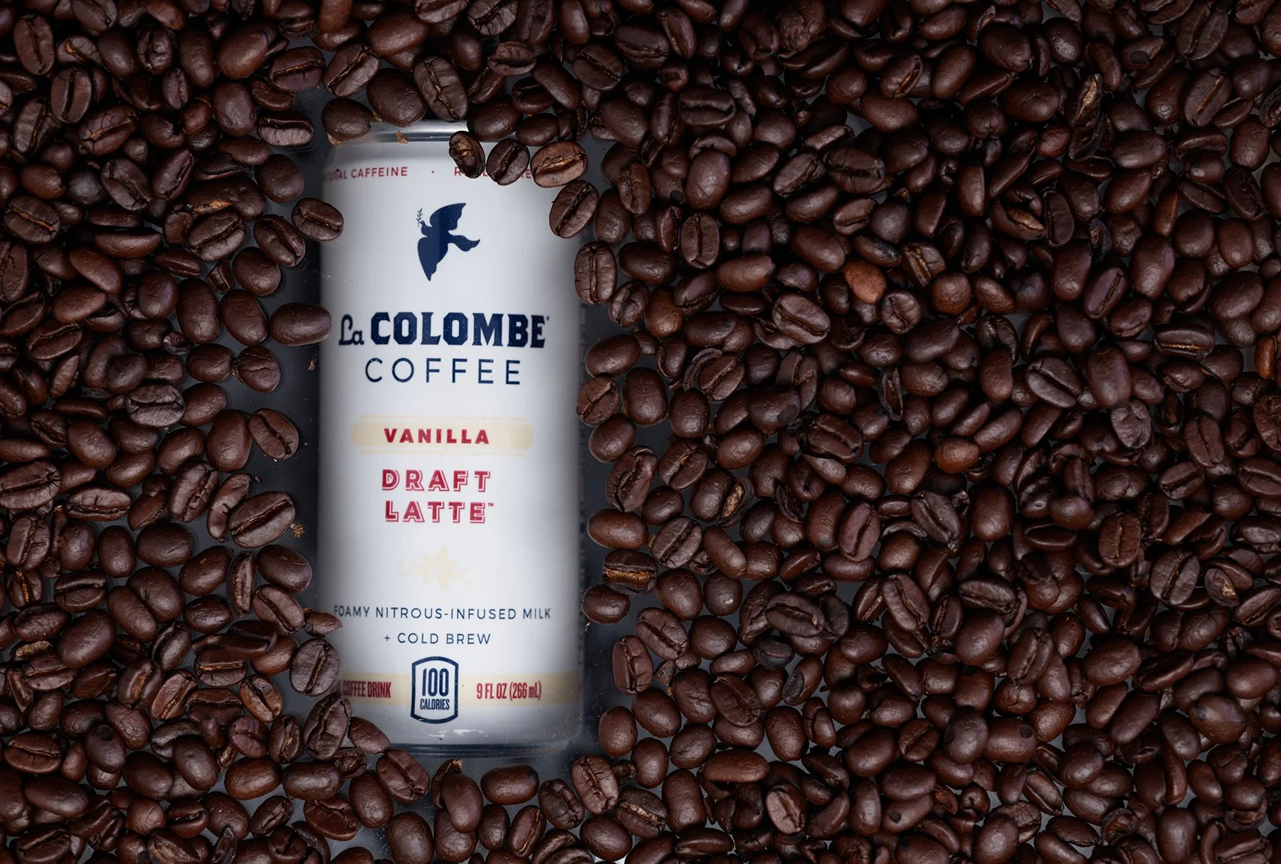 A La Colombe Vanilla Draft Latte drink can surrounded by roasted coffee beans.