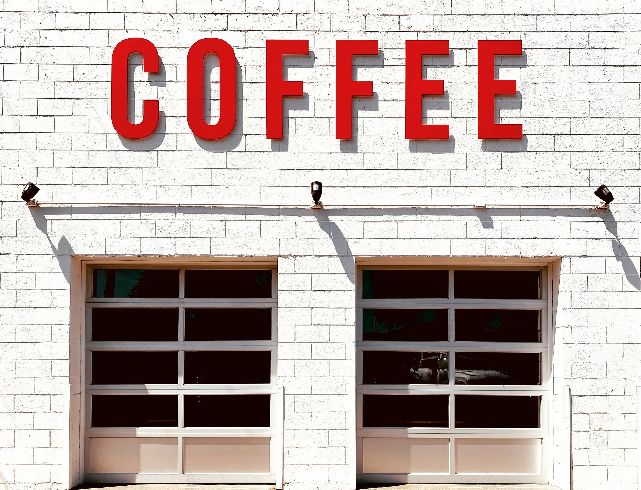 White brick building with large red letters spelling 'COFFEE' on the front and two garage doors below. Hansa Coffee in Libertyville, Illinois