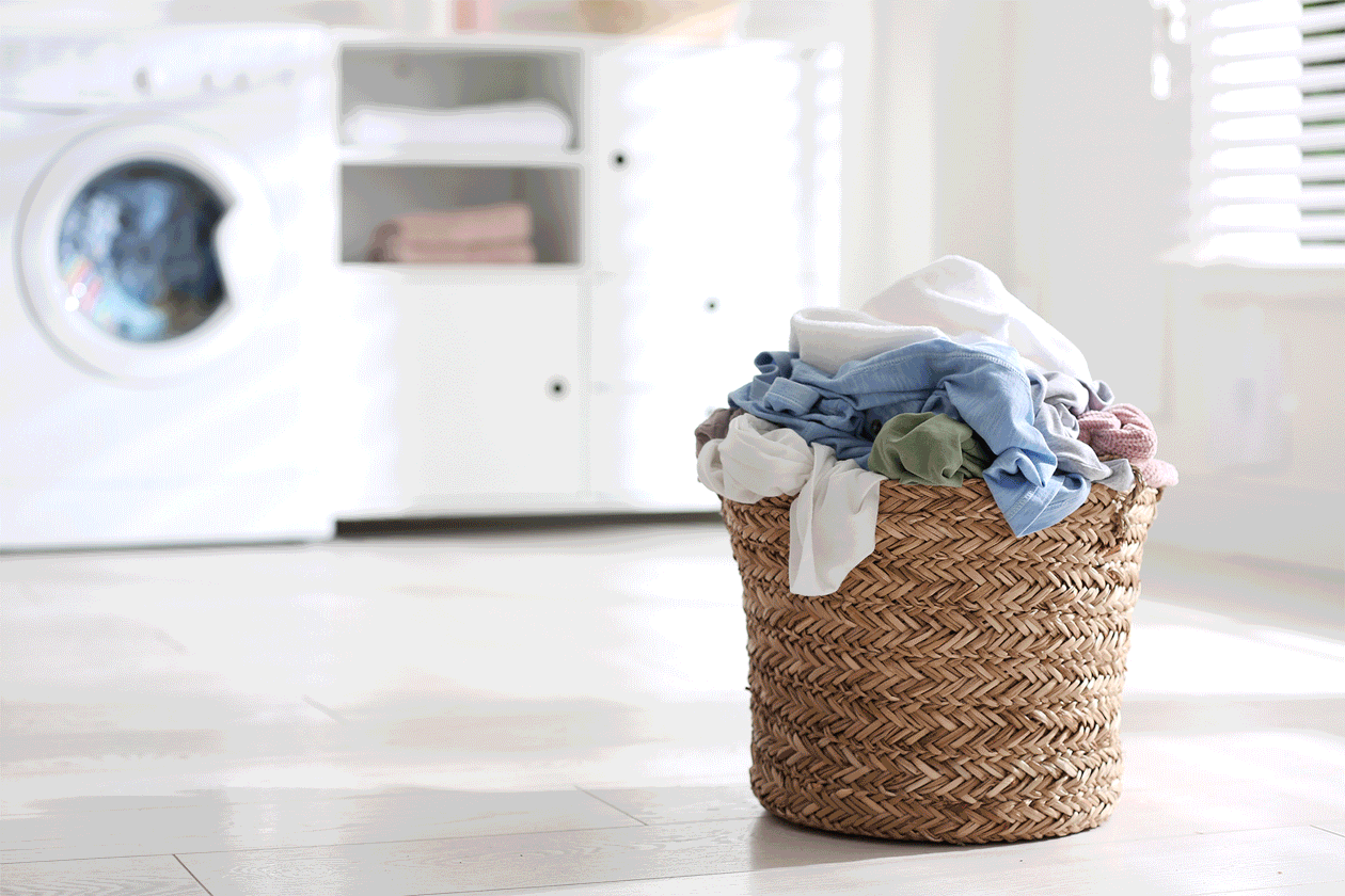 A laundry basket filled with clothes on a light-colored floor in a laundry room.
