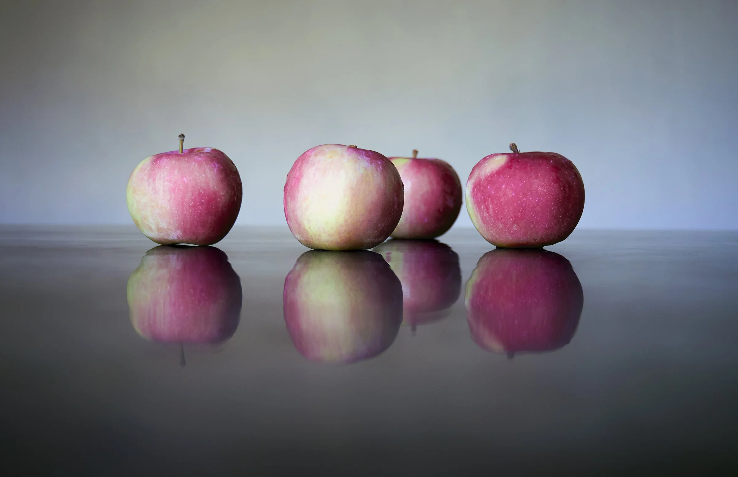 Four apples on a reflective surface with a blurred background.