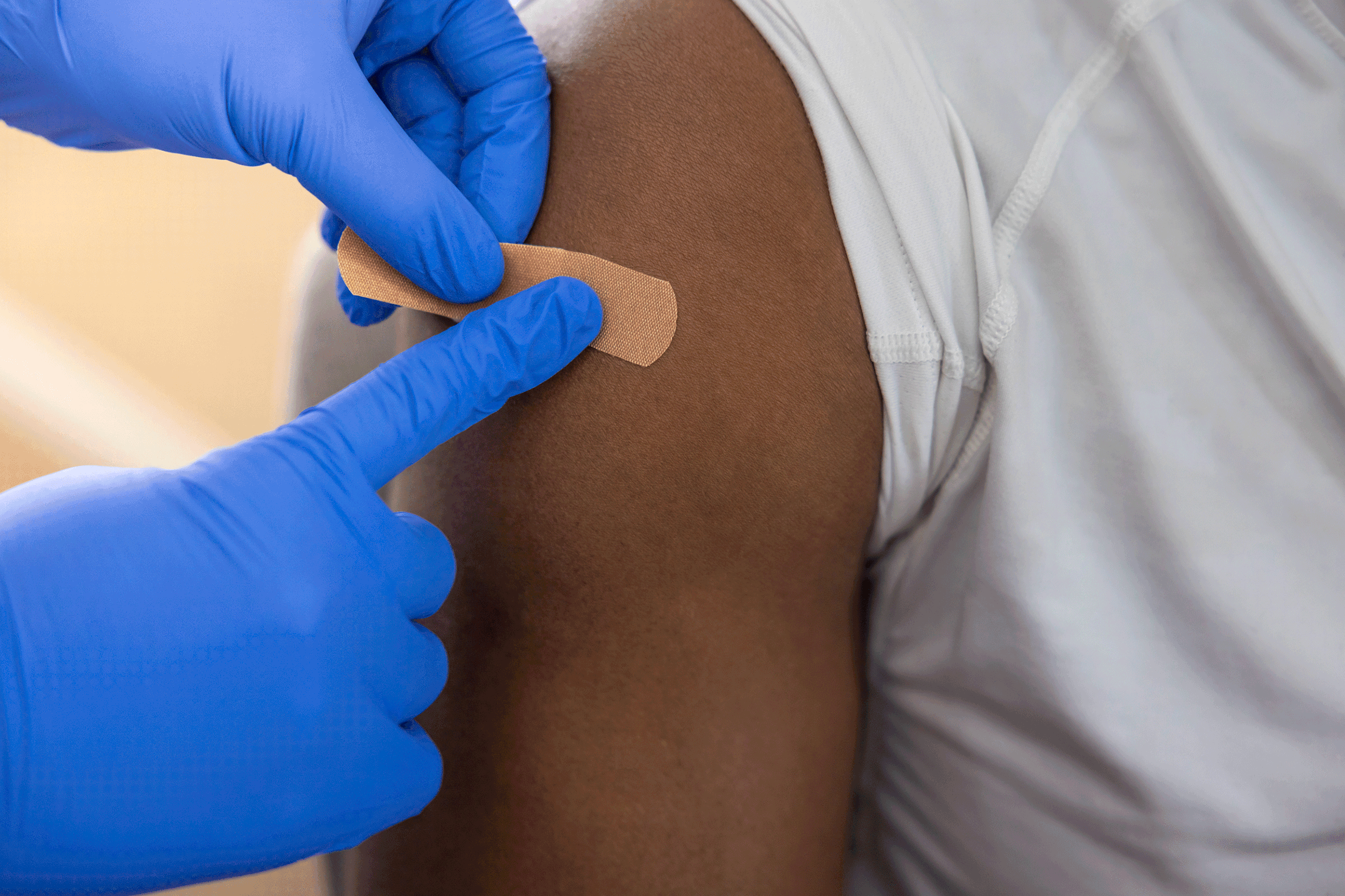 A healthcare worker wearing blue gloves applying a bandage to a person's upper arm after receiving a vaccination.