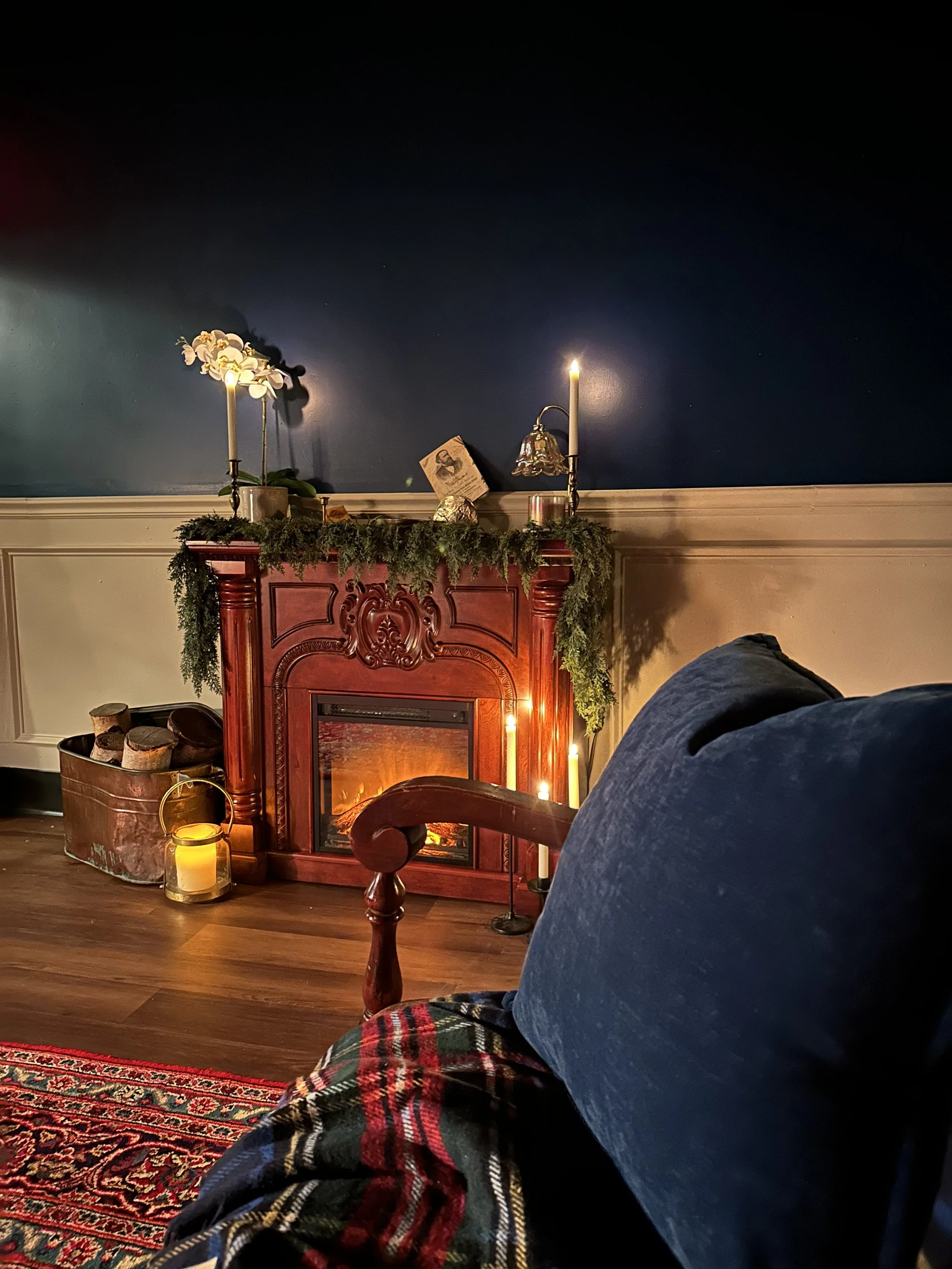 Living room with a blue wall, decorated fireplace mantel, candles, and a blue pillow on a piece of furniture in the foreground.