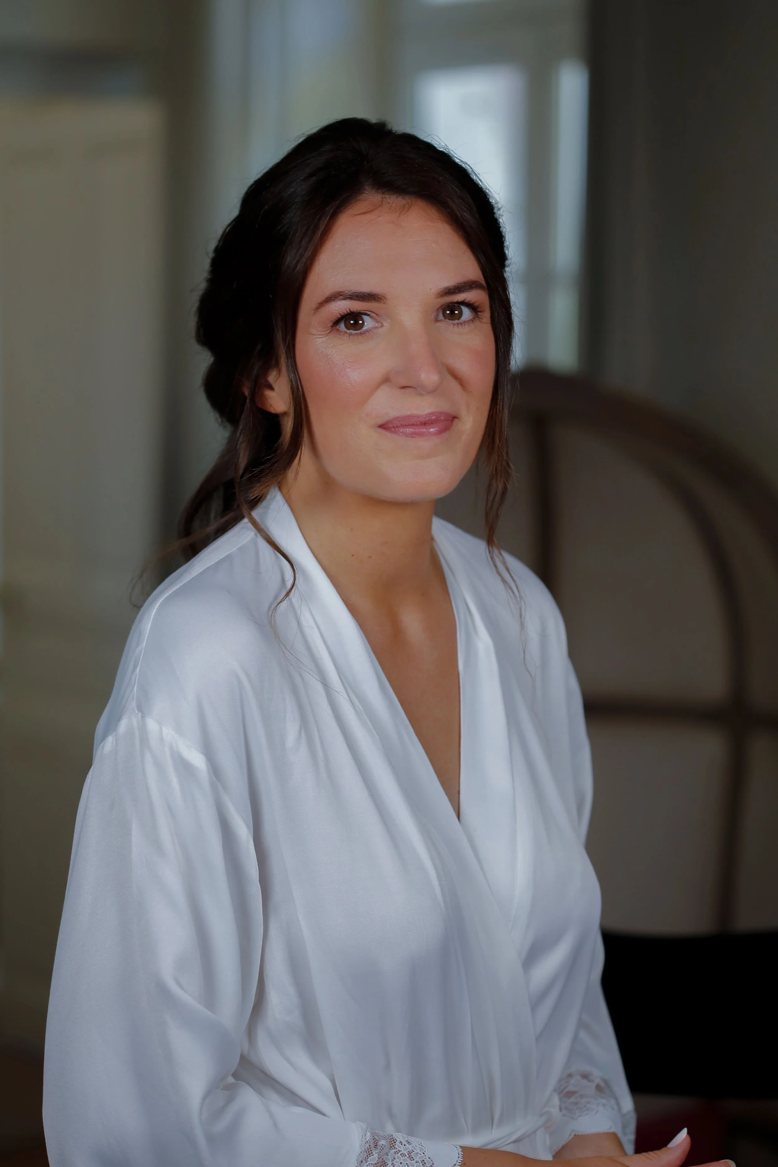 Une femme souriante portant une robe en satin blanc dans un intérieur lumineux.