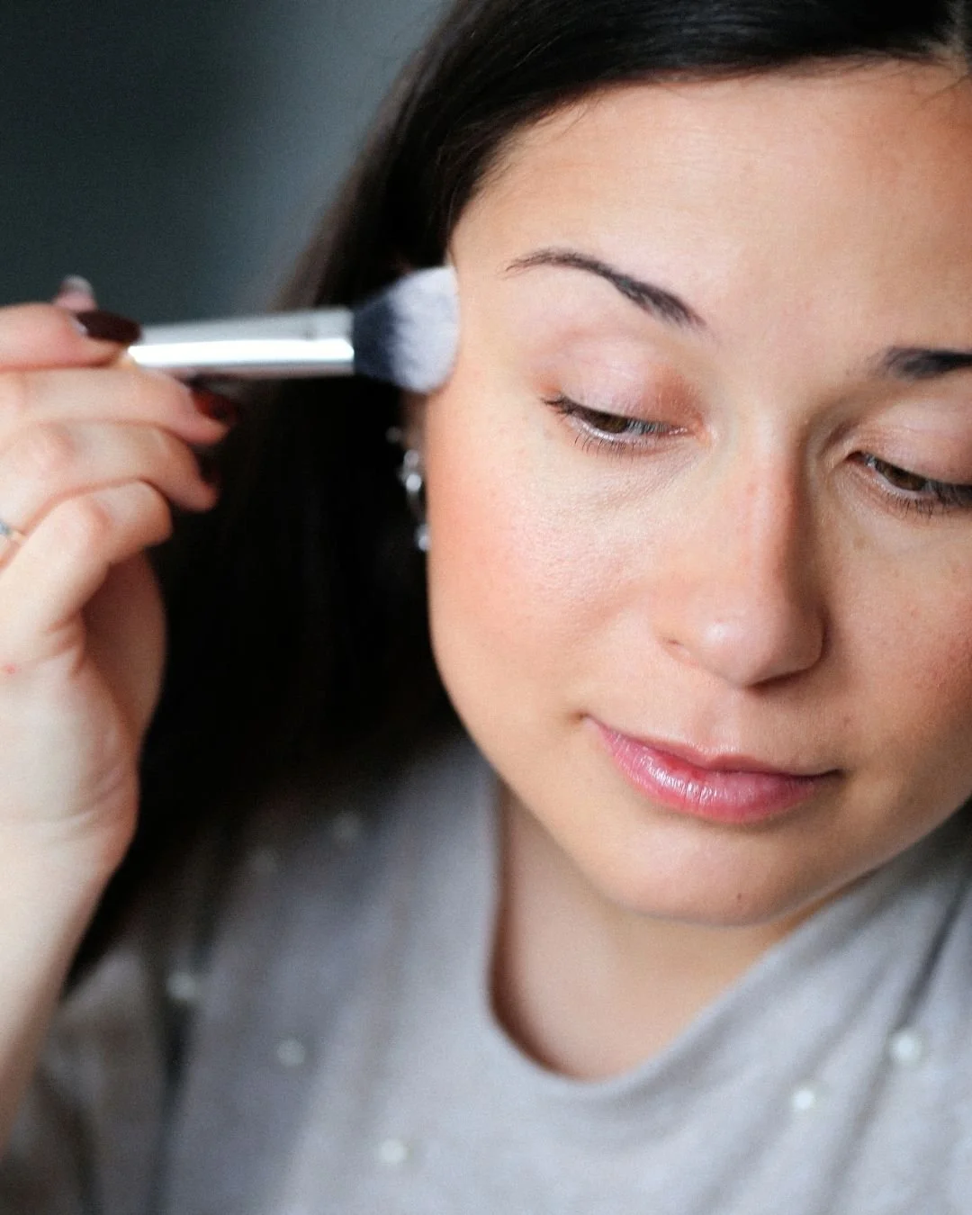 Une femme qui se maquille, utilisant un pinceau pour appliquer du maquillage sur sa joue lors d'un cours de maquillage avec un maquilleuse professionnelle en Vendée.