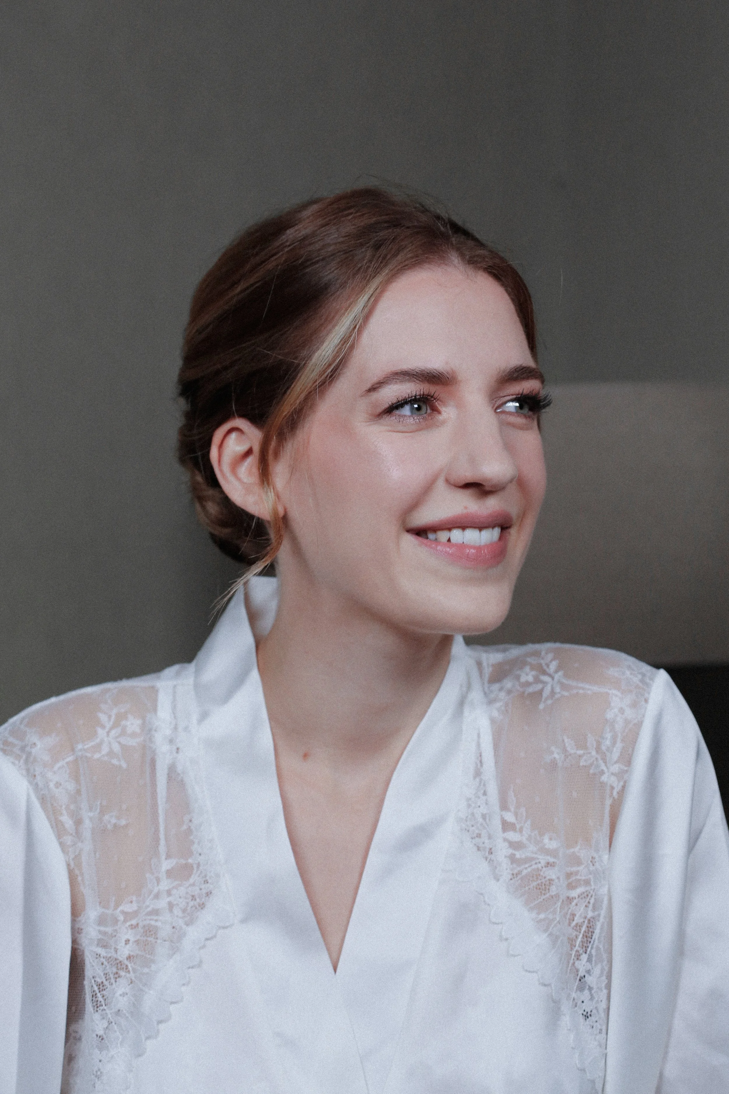 Femme souriante portant une robe ou une chemise blanche avec des détails en dentelle sur les épaules. Elle porte un maquillage naturel et élégant pour son mariage.