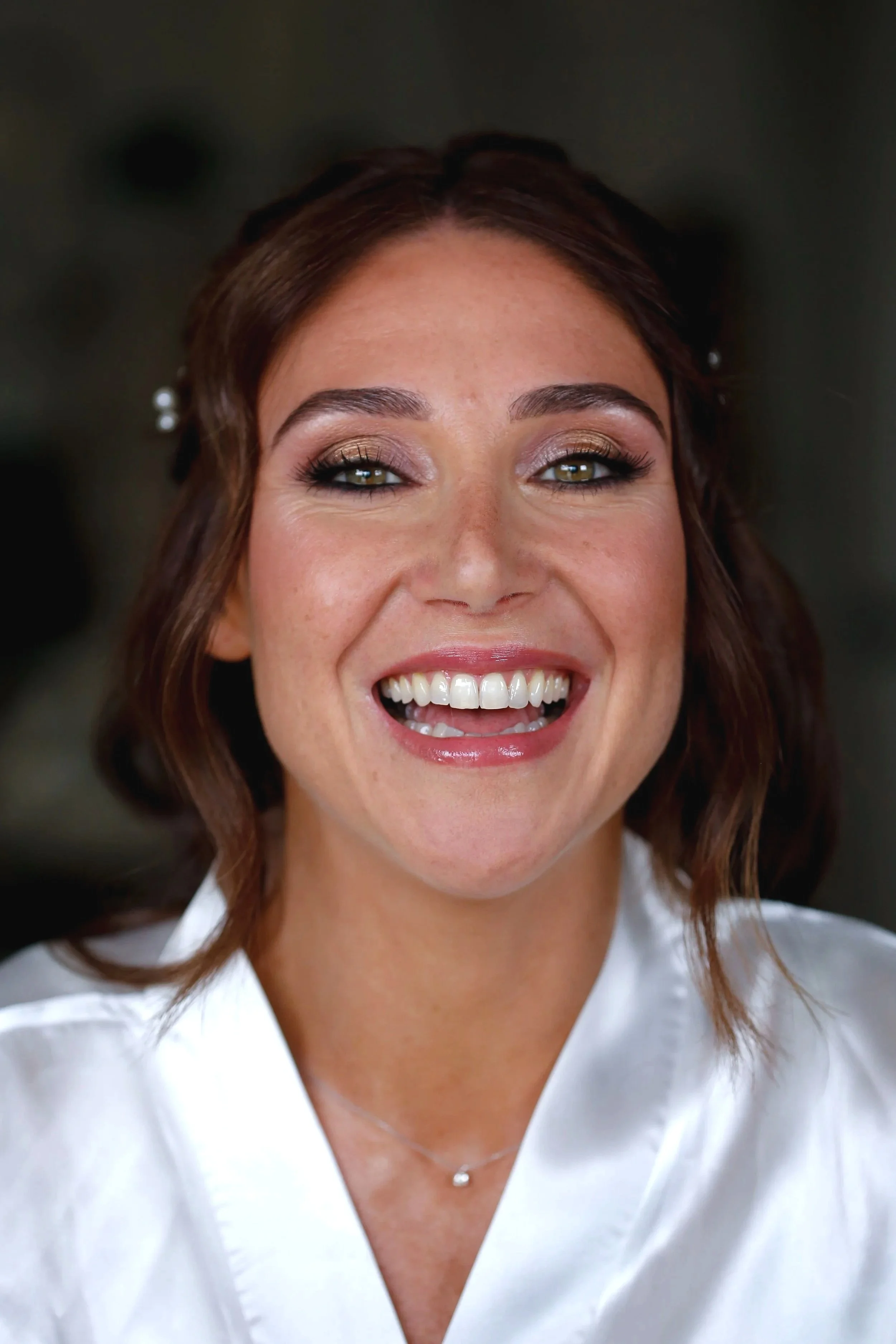 Une femme souriante avec des lèvres roses, des yeux maquillés et des cheveux bruns. Elle porte un maquillage glamour et élégant pour son mariage.