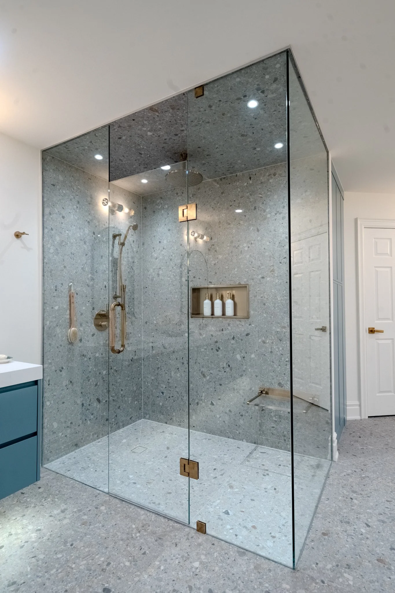Modern walk-in shower with glass walls, tiled walls, a built-in shower niche with three bottles, and recessed ceiling lights.