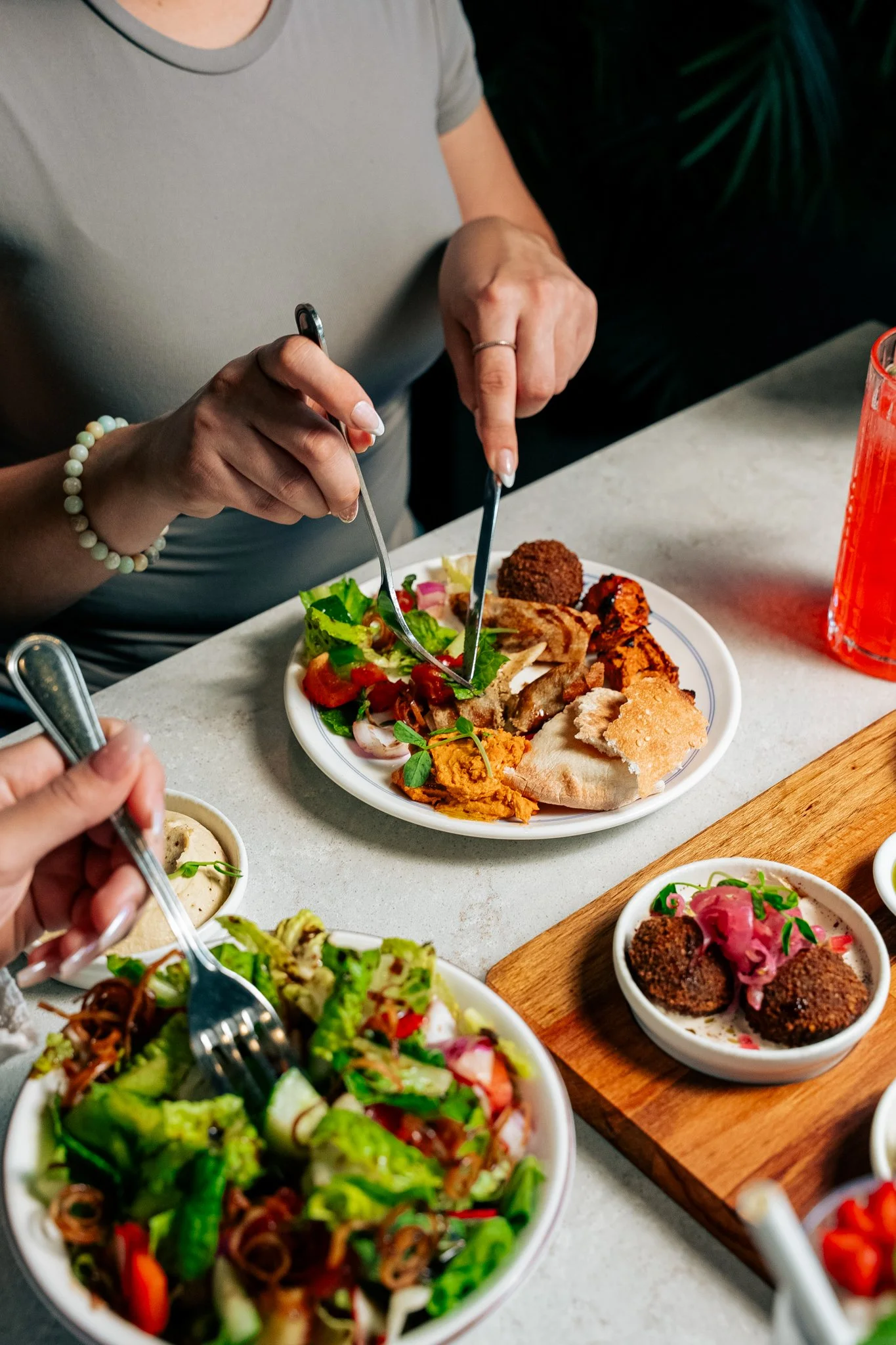 People sharing a meal at a dining table with various dishes including salads, fried appetizers, and pita bread.