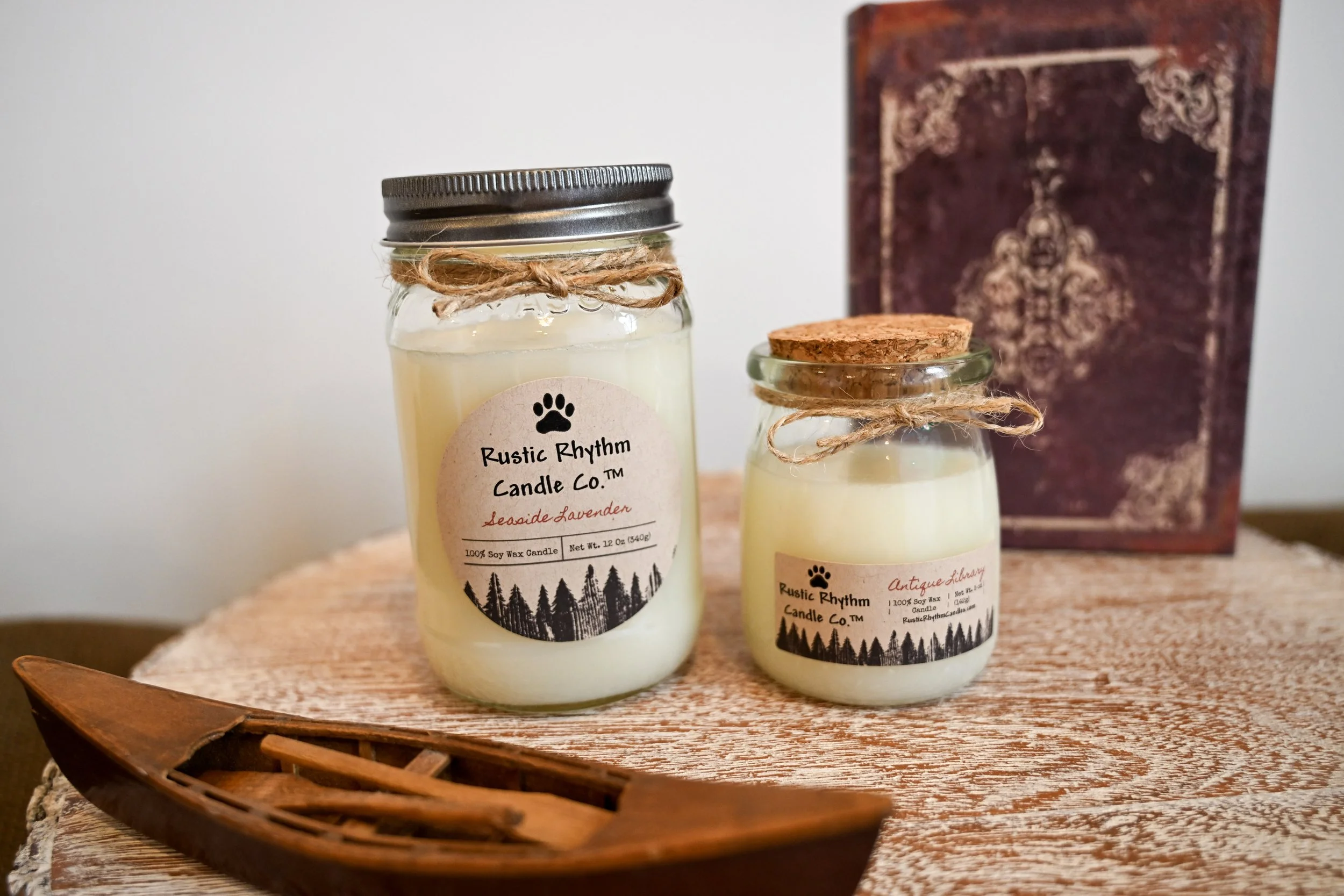 Two Rustic Rhythm Candle Co.™ candles displayed with a small canoe