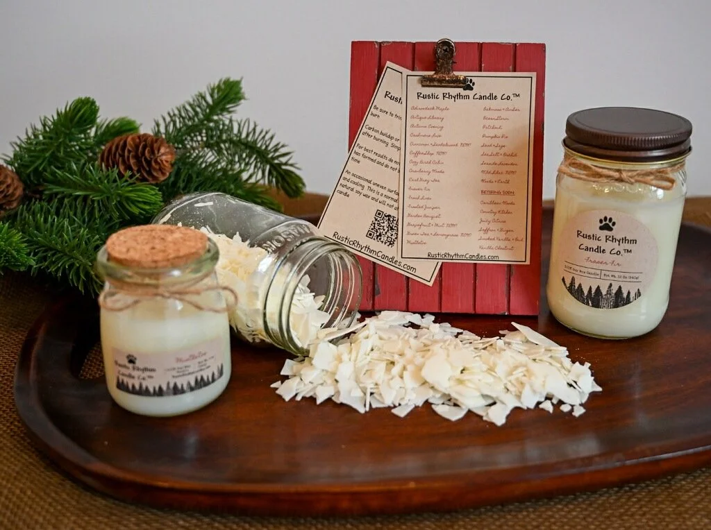raw wax pouring out of a jar with large and small Rustic Rhythm Candle Co. finished candles on a wooden board