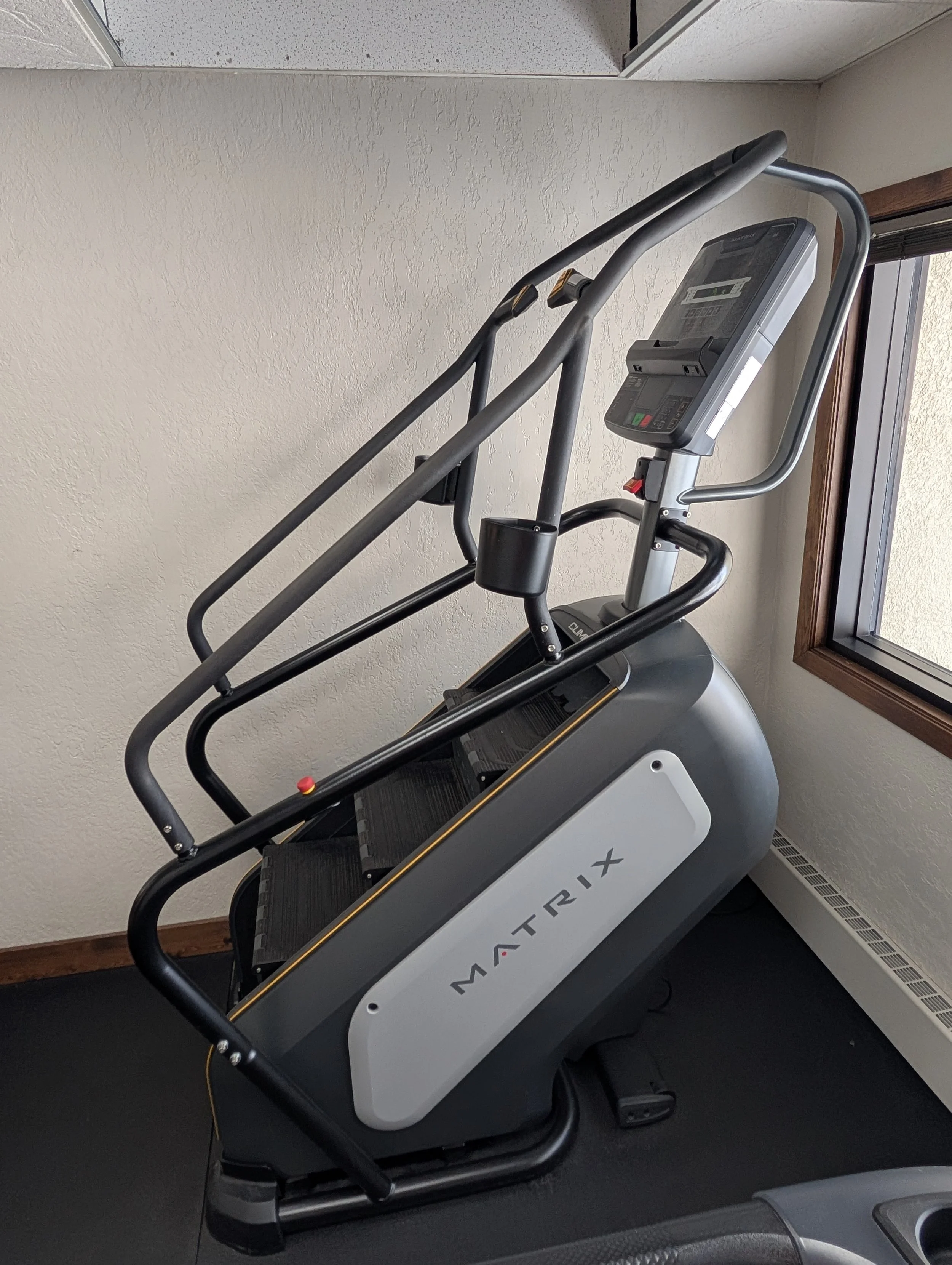 A treadmill labeled 'Matrix' positioned next to a window in a room with beige walls.