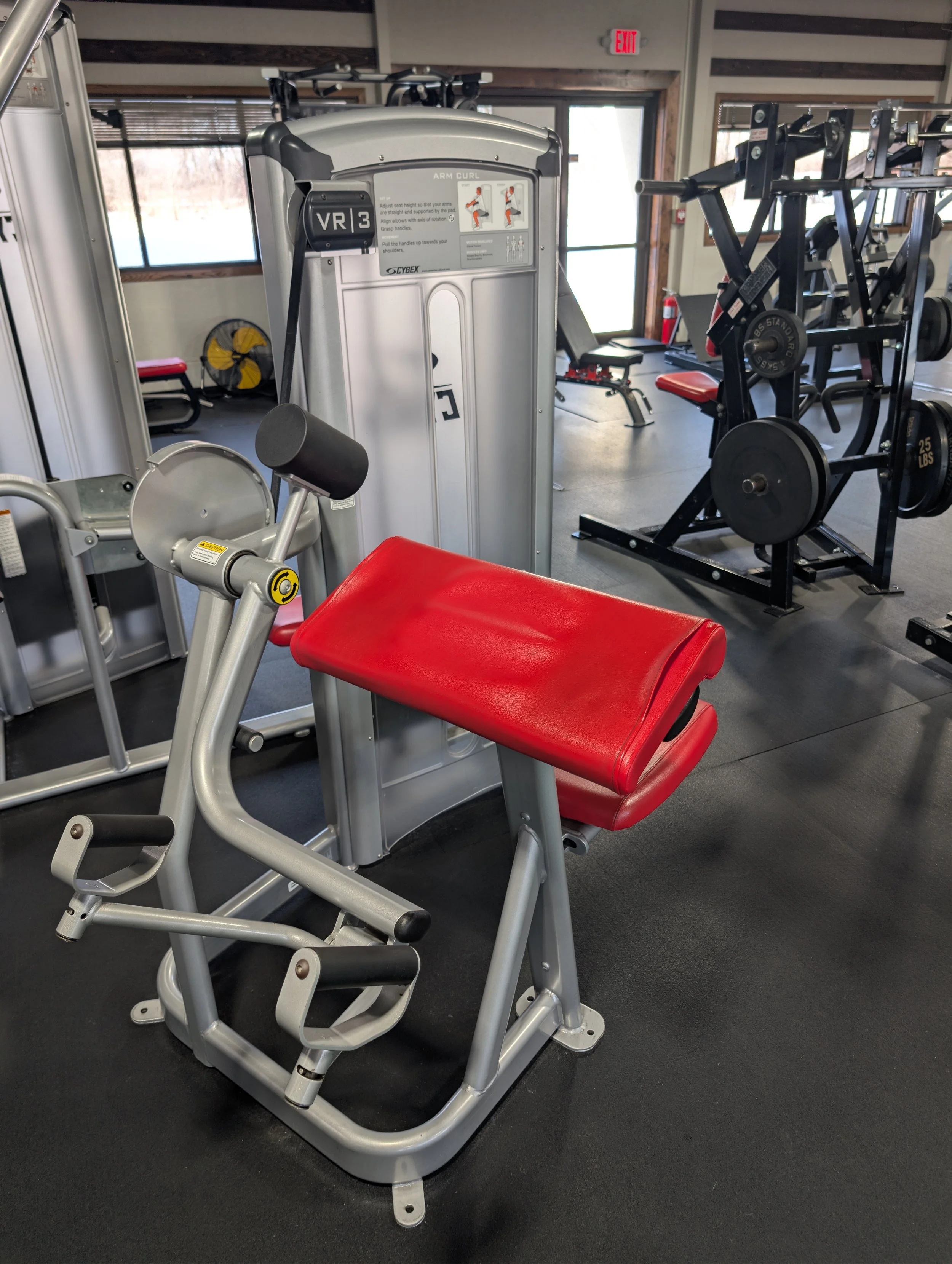 A red and gray exercise machine in a gym, with a weight station and other workout equipment in the background.