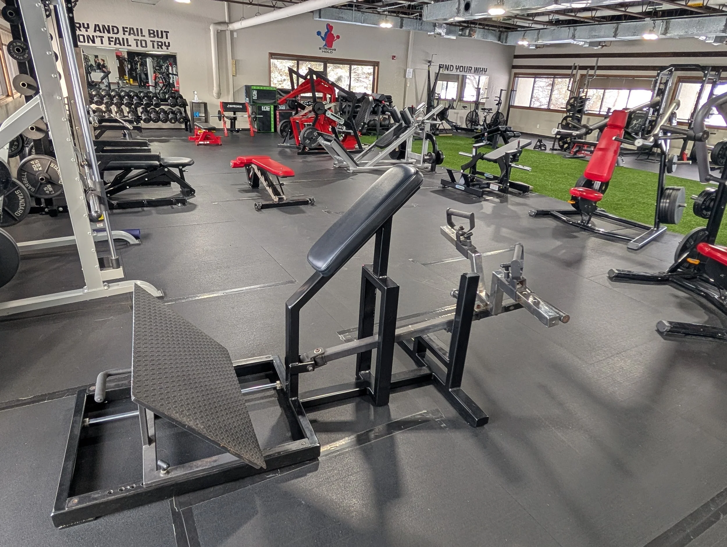 Interior of a gym with various workout equipment including benches, weights, cardio machines, and a turf area for exercises.